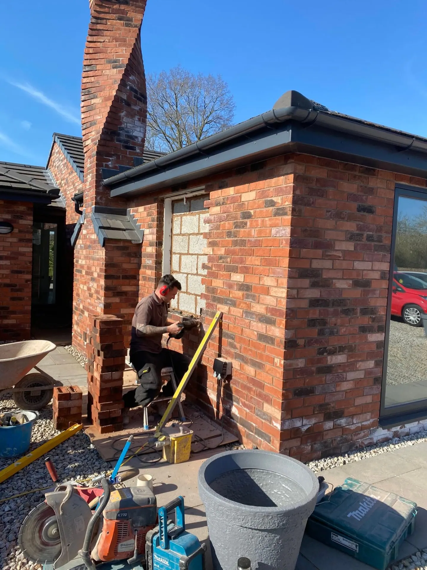 Bricklayer cutting and laying brickwork around a new window opening on a bungalow elevation with tools and a brick saw on site