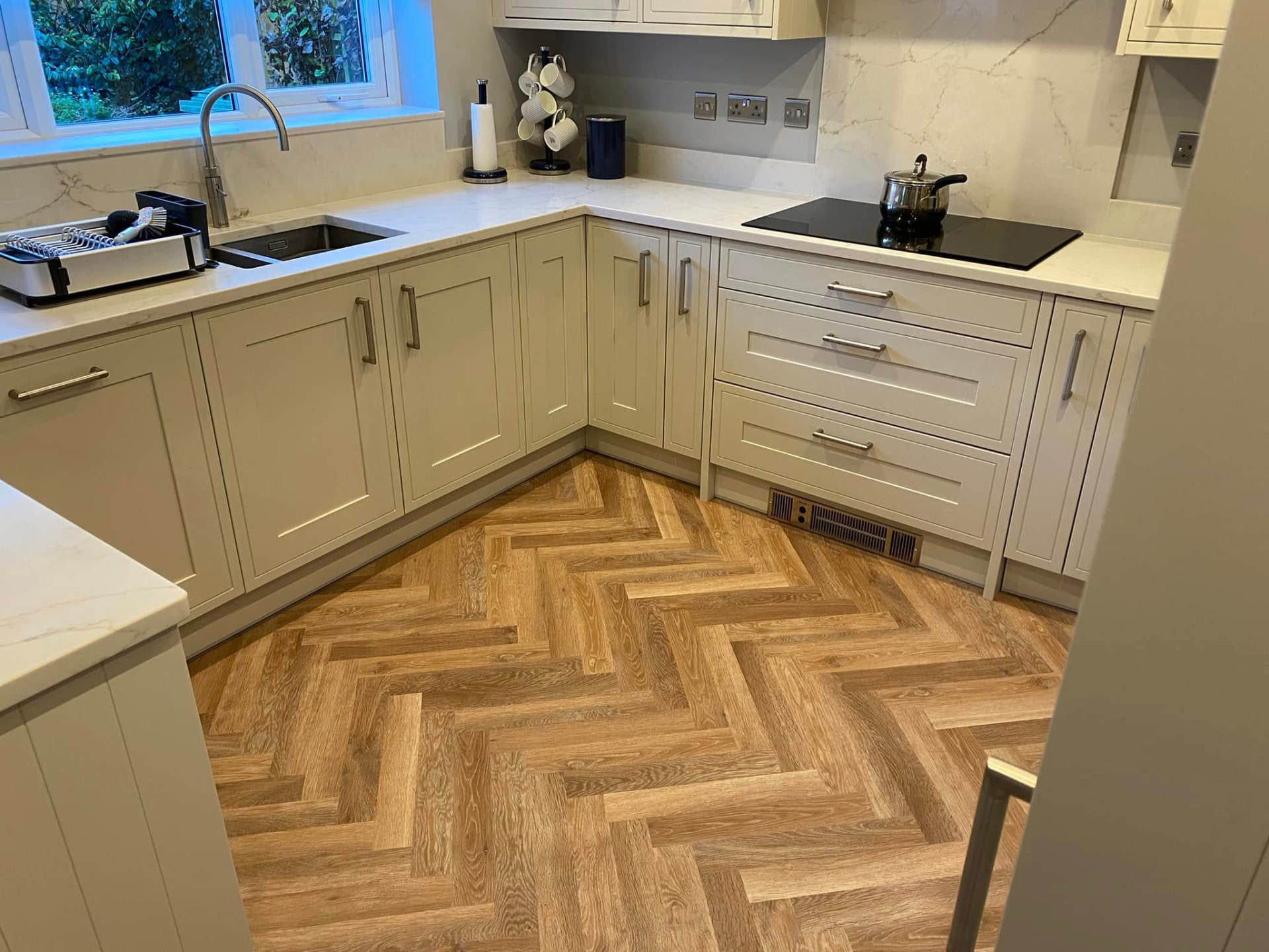 Herringbone parquet-effect flooring laid through the new kitchen against cream shaker units and quartz worktops