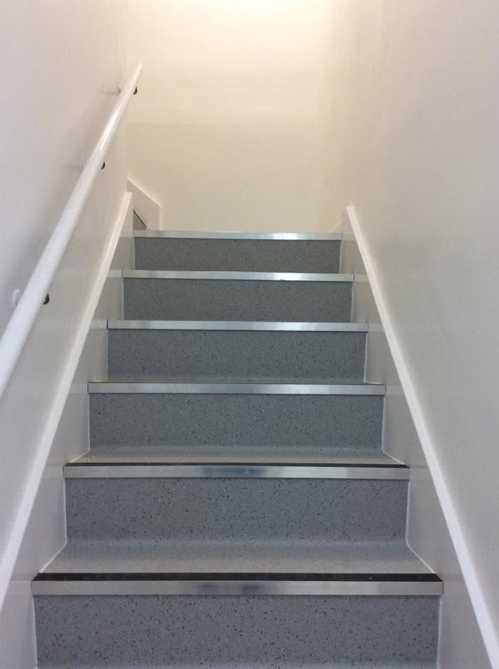 Staircase finished in speckled hygienic sheet vinyl with stainless nosings and a white handrail