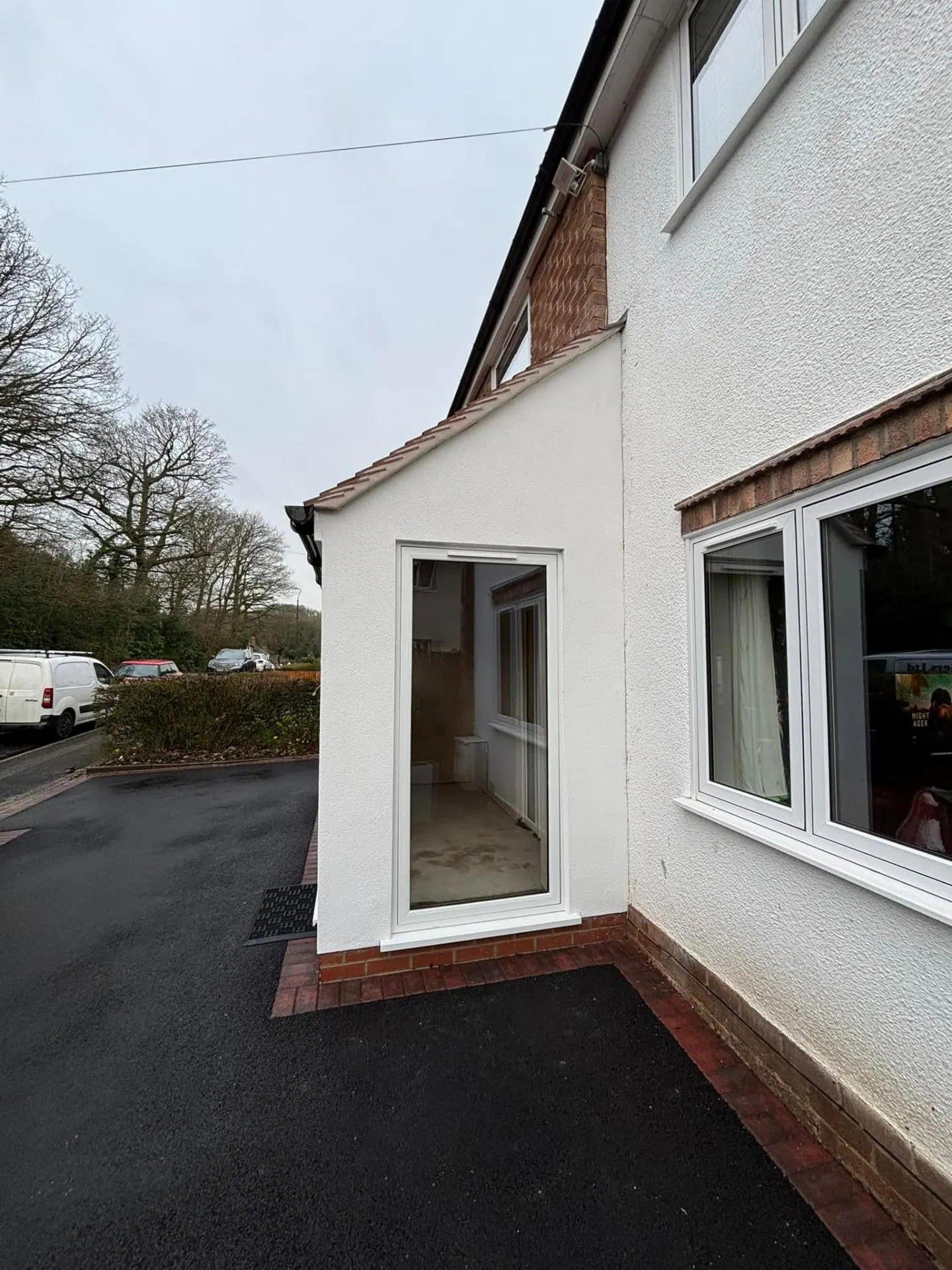Close-up of the full-height glazed side return of the new Redditch porch with brick plinth meeting the new tarmac driveway