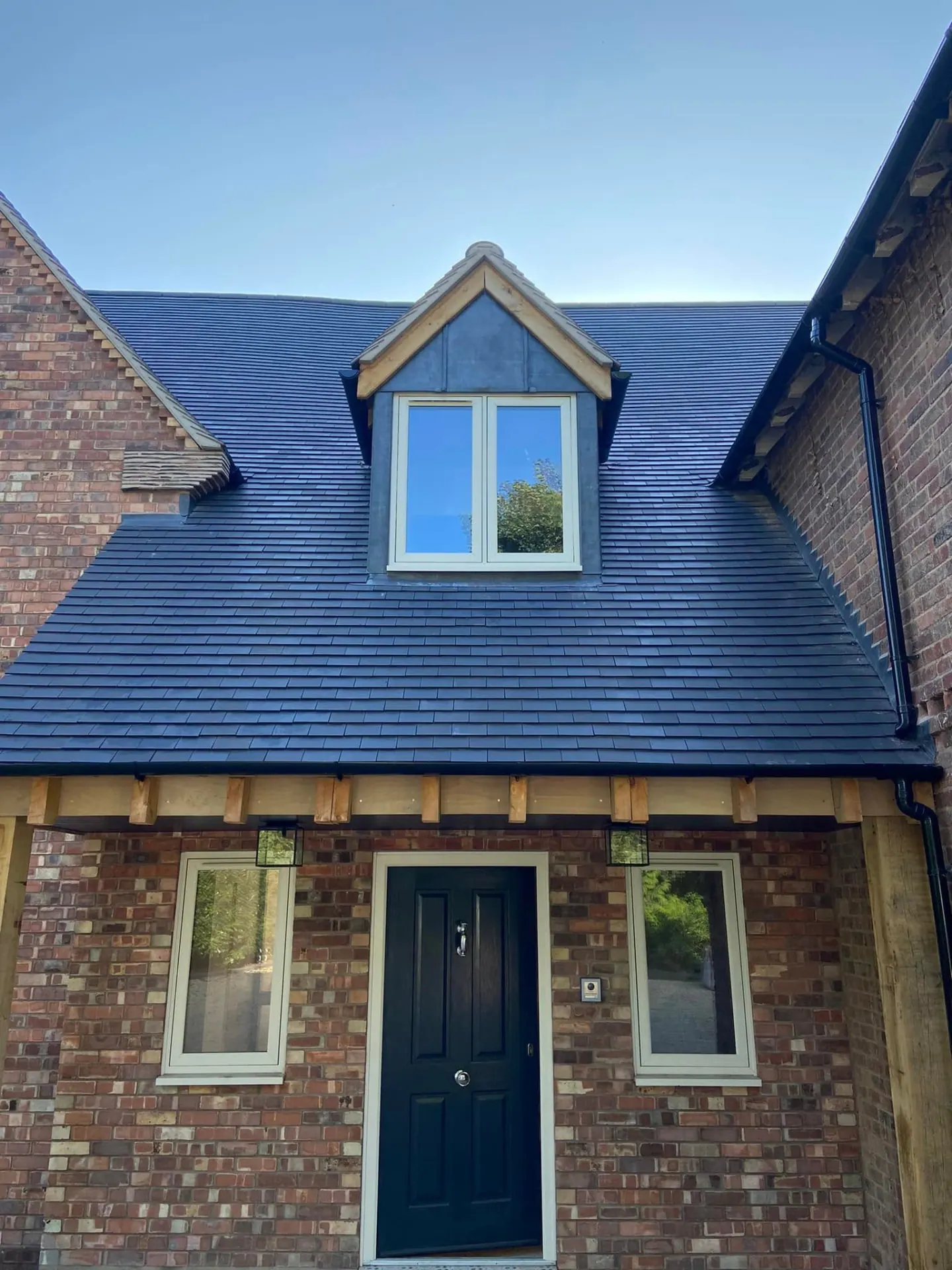 Close view of the finished front entrance with dark front door, dormer above and brick detailing beneath the slate roof