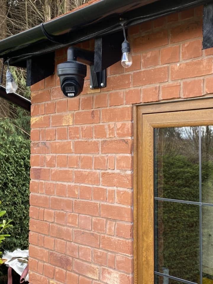 CCTV camera and festoon lighting mounted on the brick corner of the man cave beneath black rainwater goods