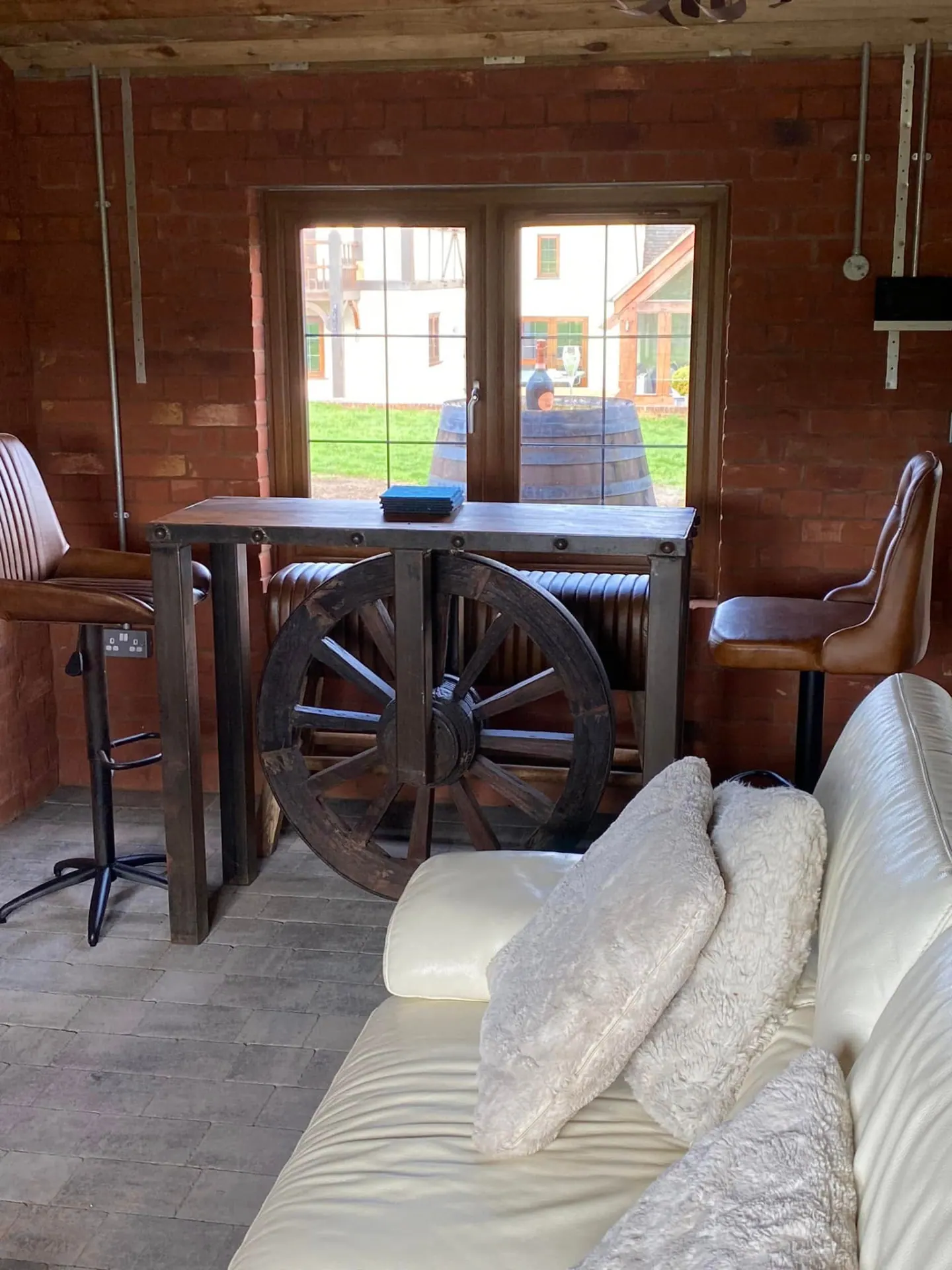 Bar height table with leather stools and a vintage wagon wheel against the exposed brick wall of the man cave