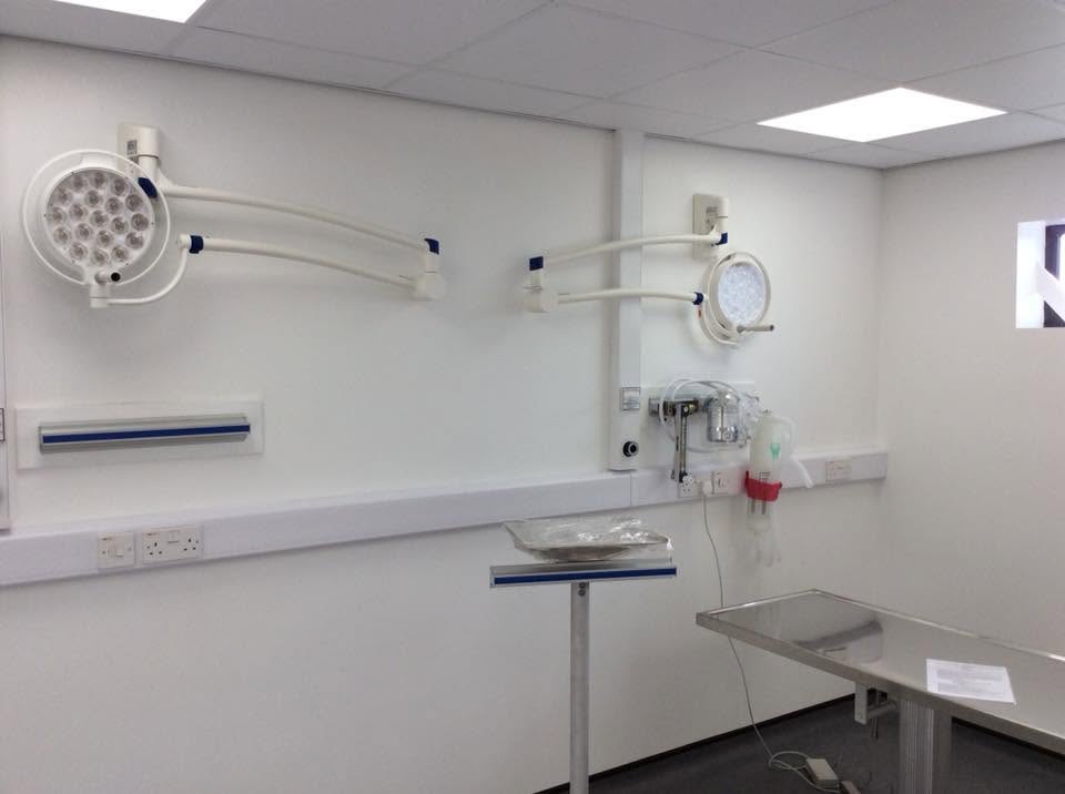 Veterinary operating theatre with two wall-mounted pendant LED operating lights, medical gas points, hygienic wall sheeting and a stainless operating table