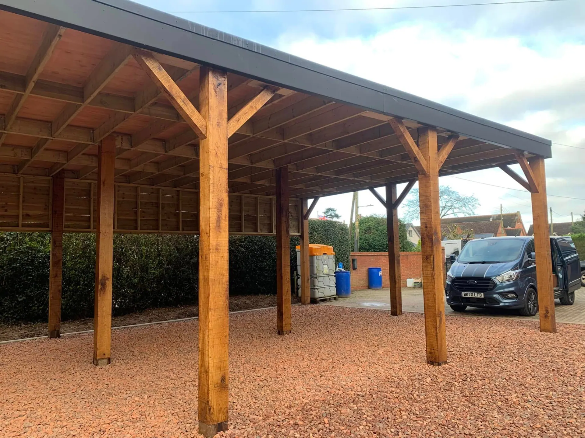 Oak tractor port frame showing heavy posts, angled braces and the steel roof edge from the side