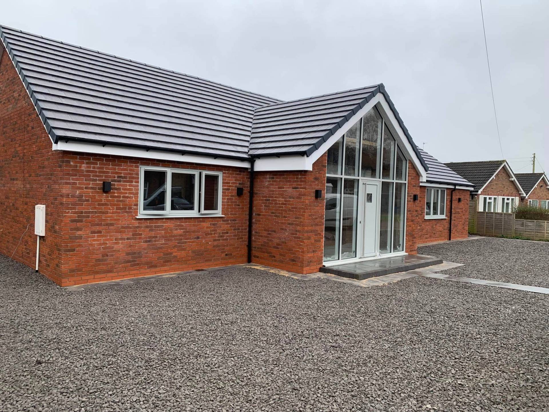 Finished front elevation of White Gates in Worcestershire — a tired two-bed bungalow transformed by JRC Developers into a modern three-bedroom home with red brick walls, grey plain tile roof and a full-height glazed gable entrance