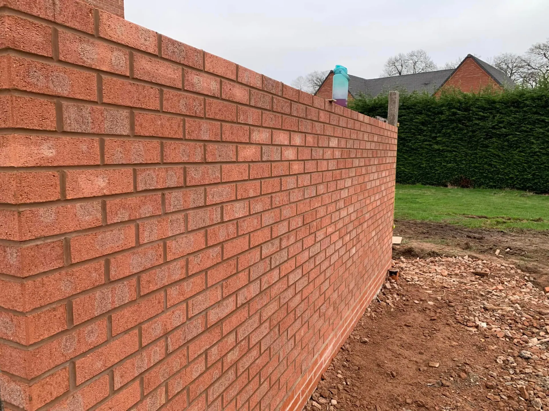 Long run of matched red brick boundary wall built to a string line beside the garden