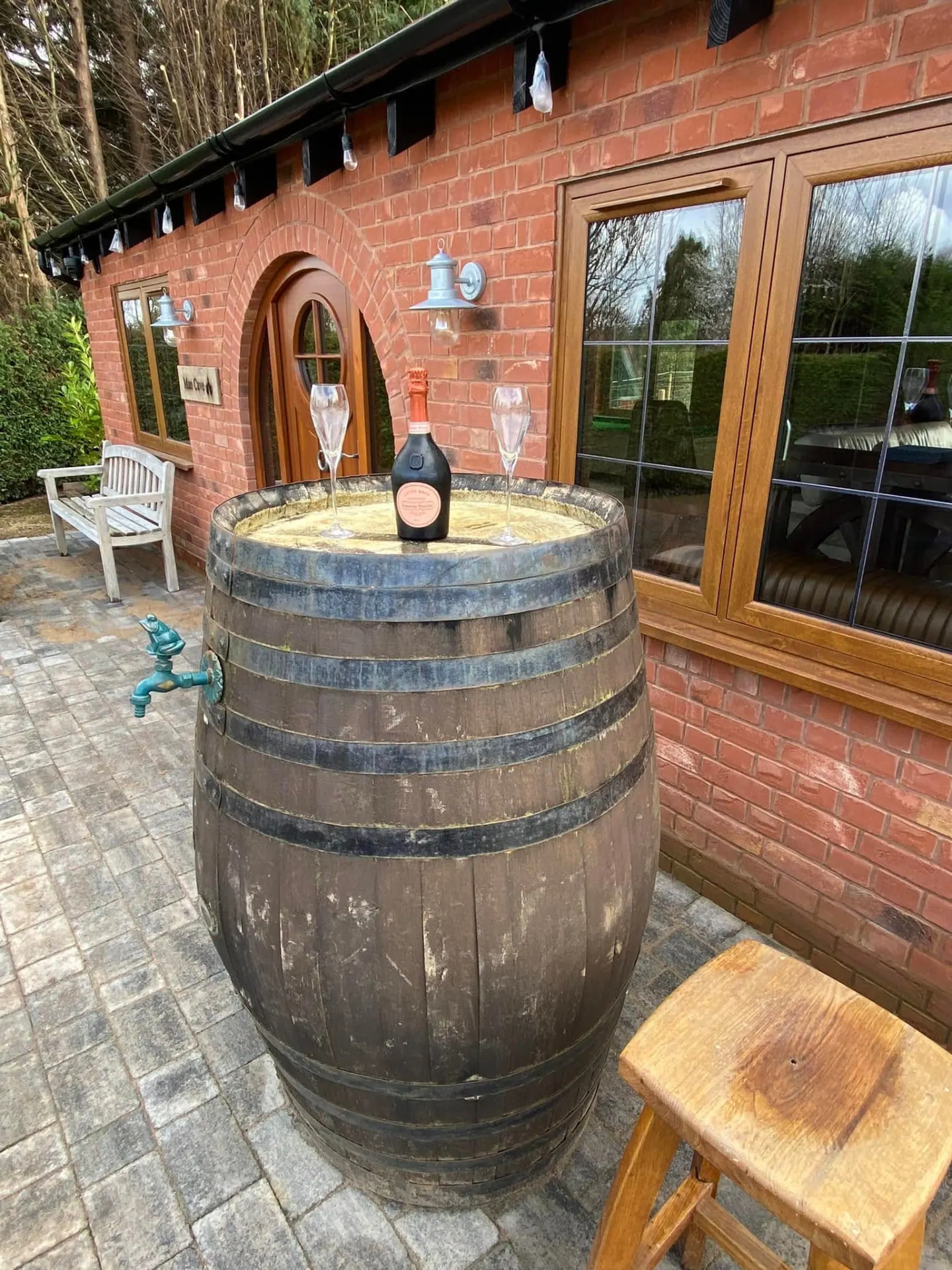 Whisky barrel table with champagne and glasses on the block paved terrace outside the finished brick man cave
