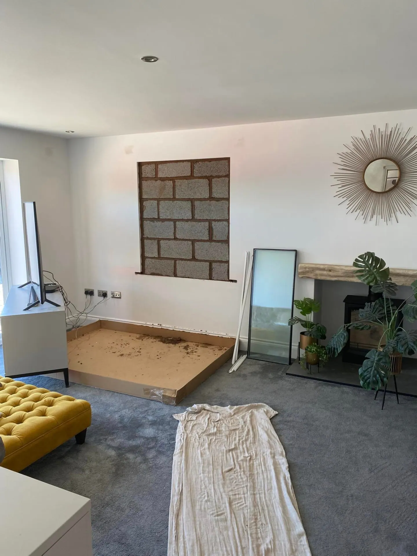 Interior lounge view of a blocked-up window opening in blockwork with the carpet sheeted and furniture protected during alterations