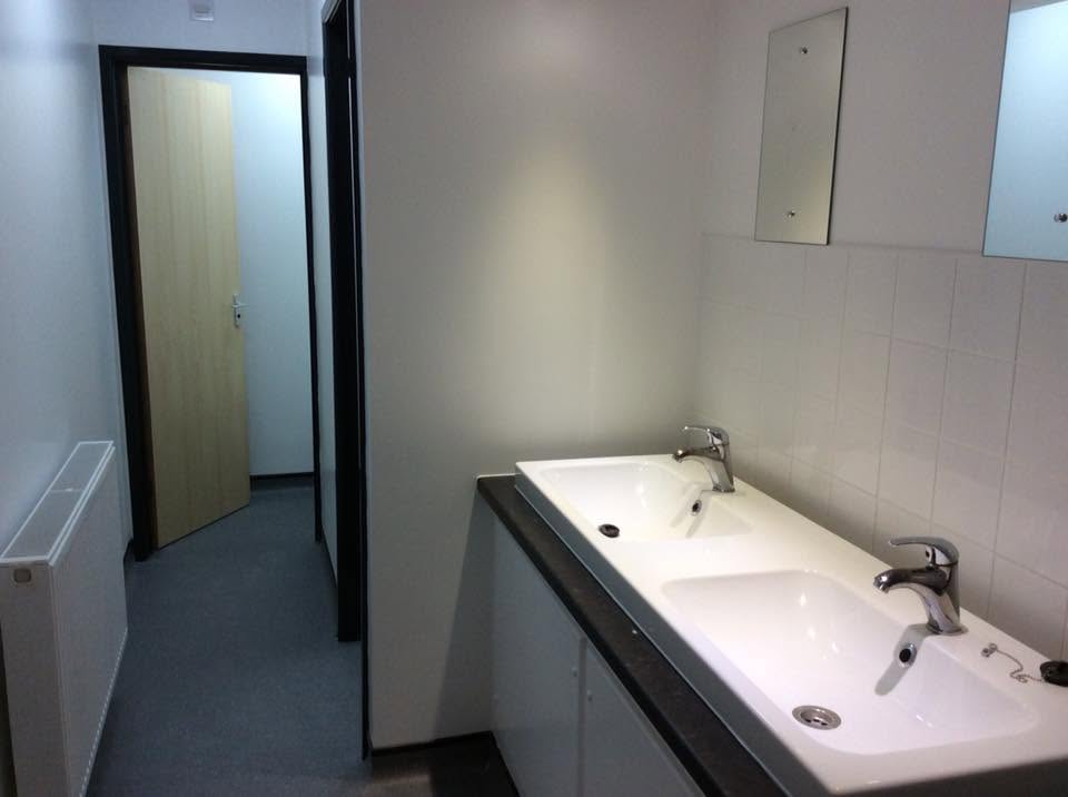 Washroom with twin white basins set into a dark worktop vanity, tiled splashback, mirrors and cubicle doors