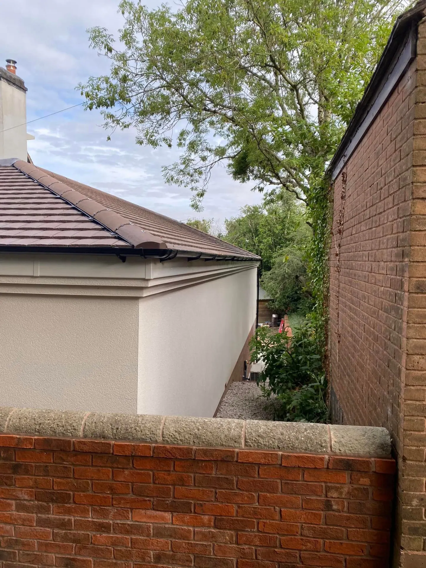Detail of the smooth off-white render, boxed eaves and clay tiled hipped roof on the new build at Whiteoaks