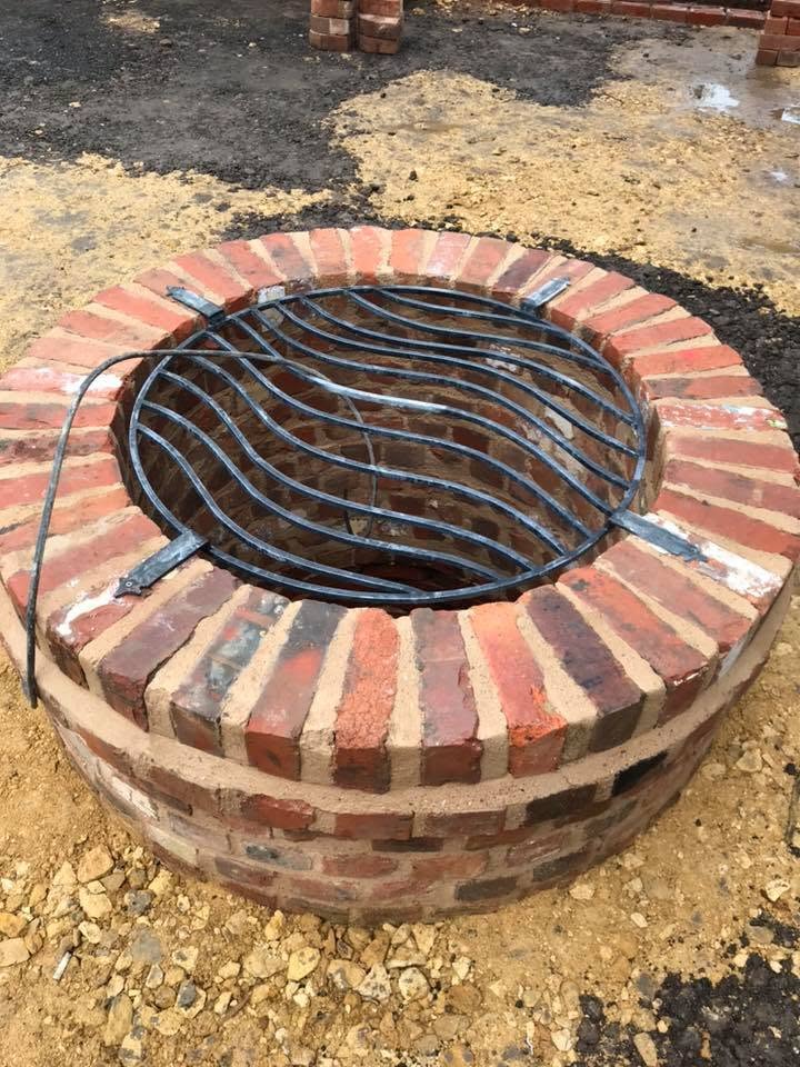 Rebuilt well head at the listed farmhouse — circular reclaimed brick surround with radial soldier-course cope and a bespoke curved steel safety grille