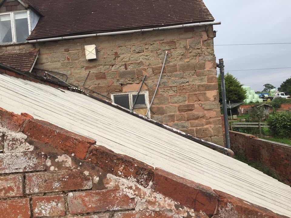 Lean-to roof being stripped away from the sandstone elevation of the listed farmhouse, exposing coursed stonework and historic brick repairs