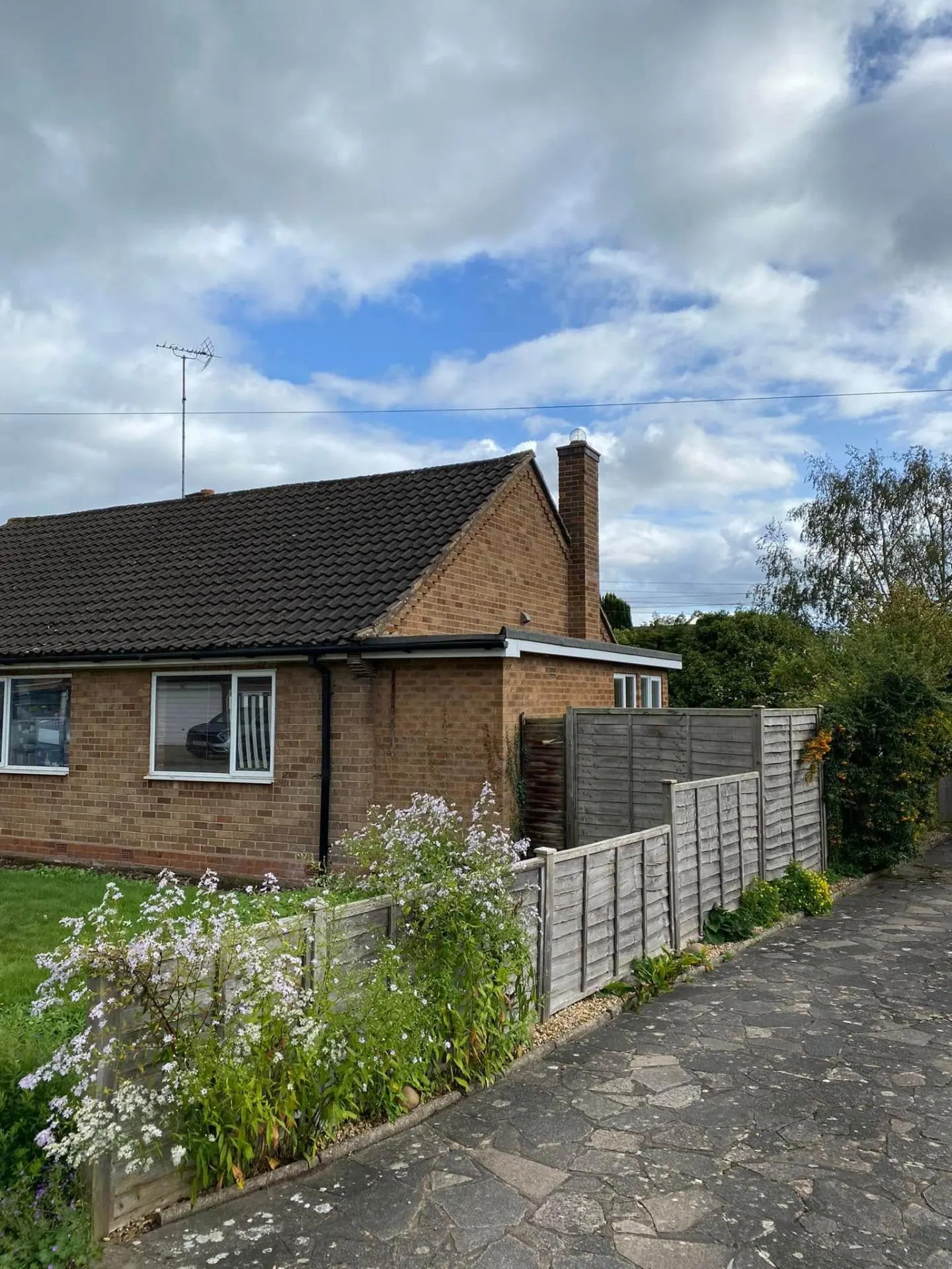 Original side elevation of the White Gates bungalow before transformation showing dated brickwork, chimney and weathered timber fence