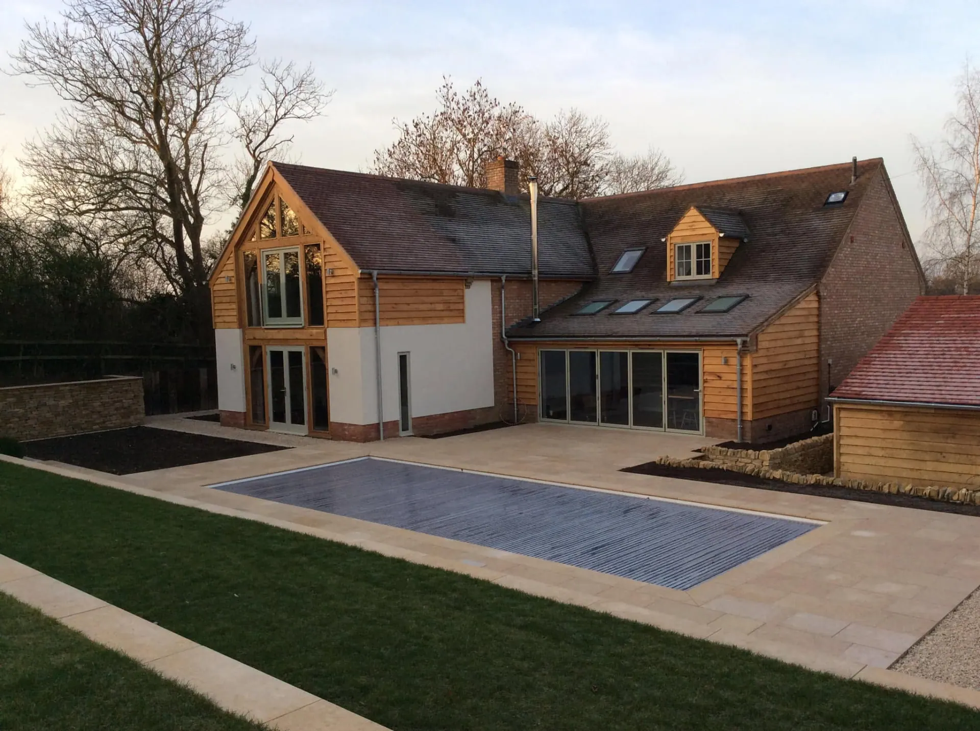 Willow House after remodelling by JRC Developers — oak-framed gables, oak weatherboard cladding and white render with a swimming pool and limestone terrace in the foreground