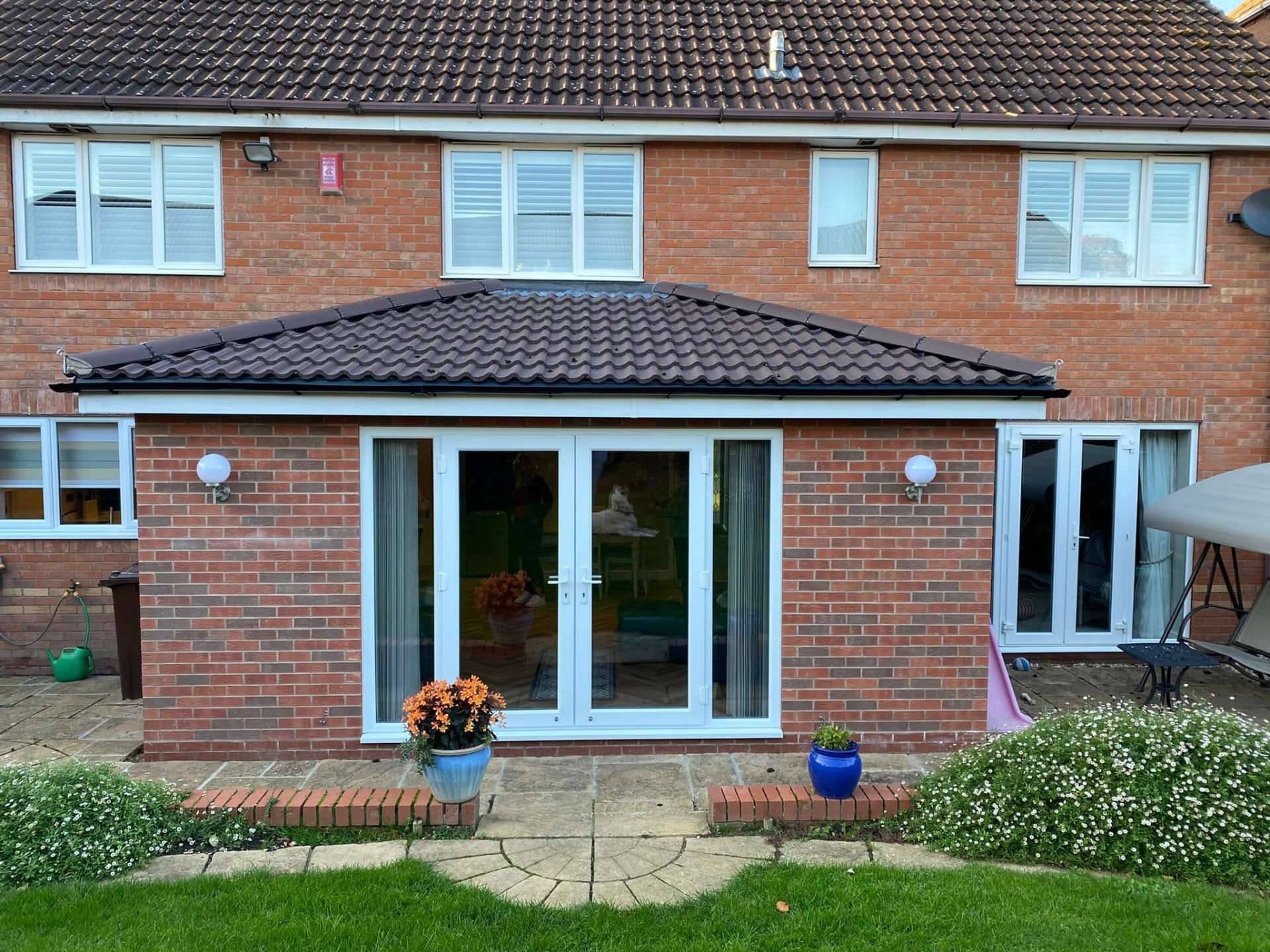 Rear brick kitchen and dining extension with a hipped brown tiled roof and white French doors opening onto a sandstone patio