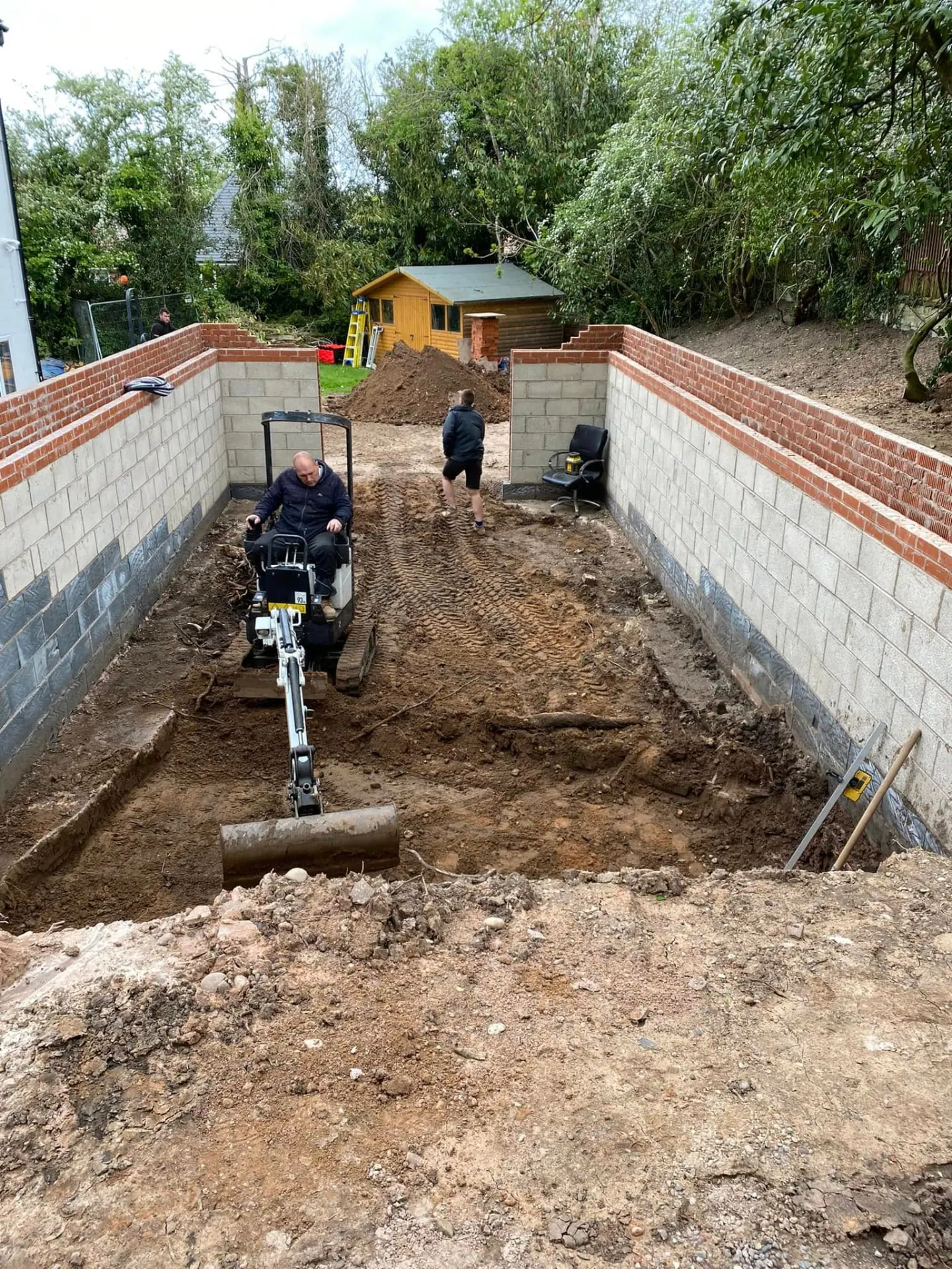 Mini excavator digging out the annexe footprint at Whiteoaks between new blockwork retaining walls with tanking and brick capping above
