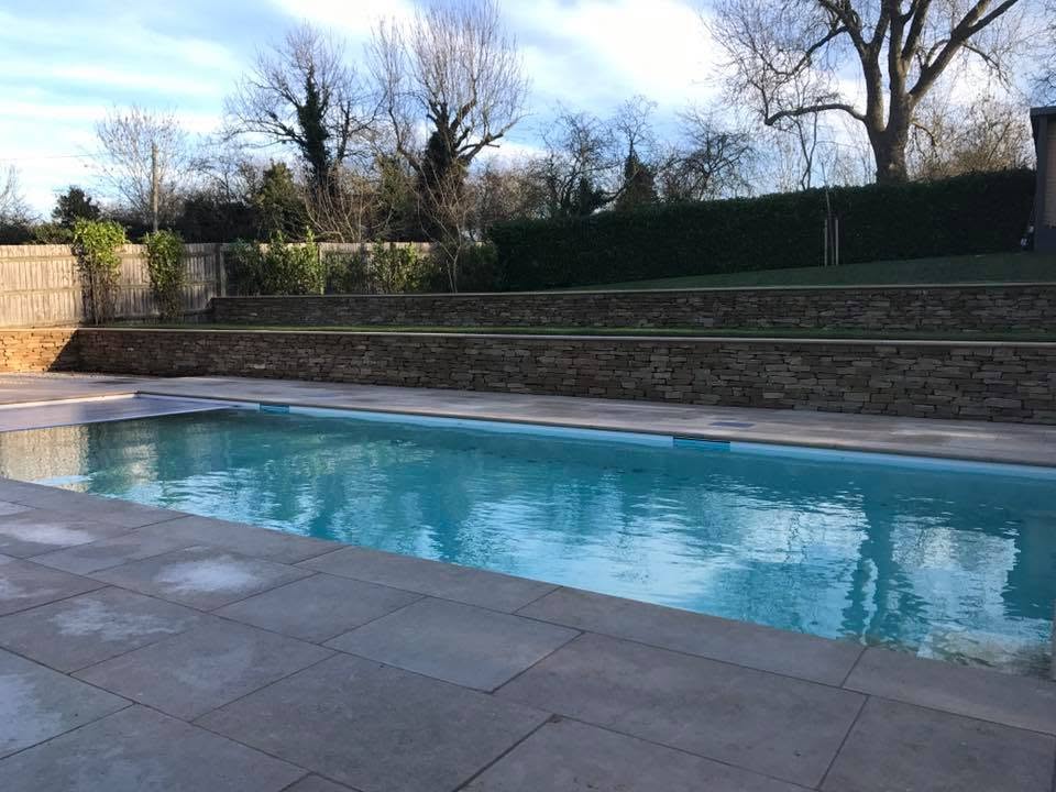 Swimming pool filled with water with a dry stone retaining wall and lawn terrace behind