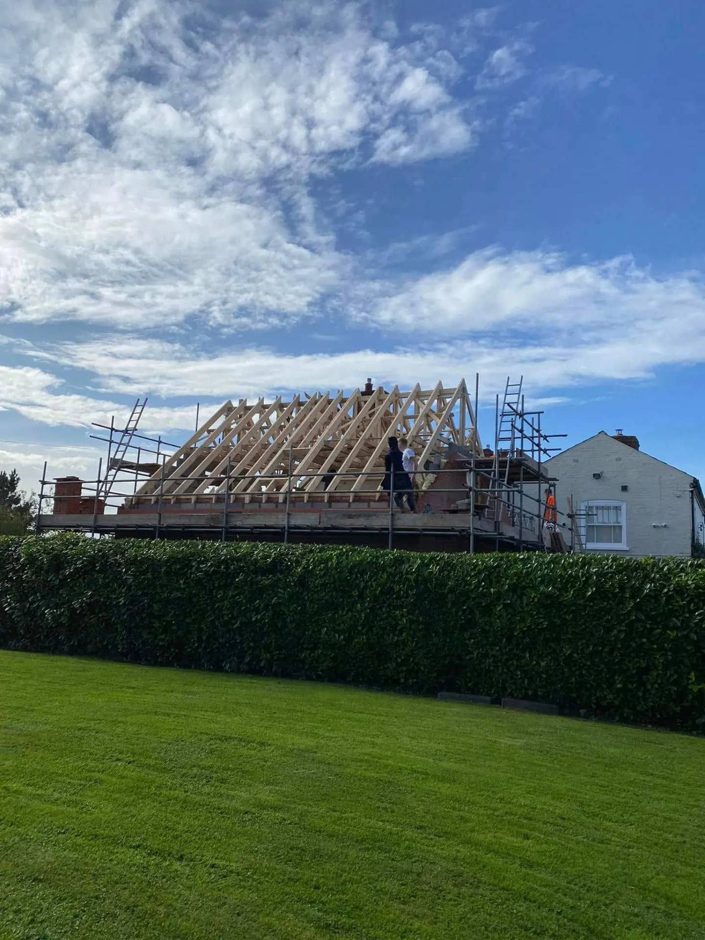 Completed hand-cut hipped timber roof frame on a farmhouse extension by JRC Developers, viewed from the front lawn