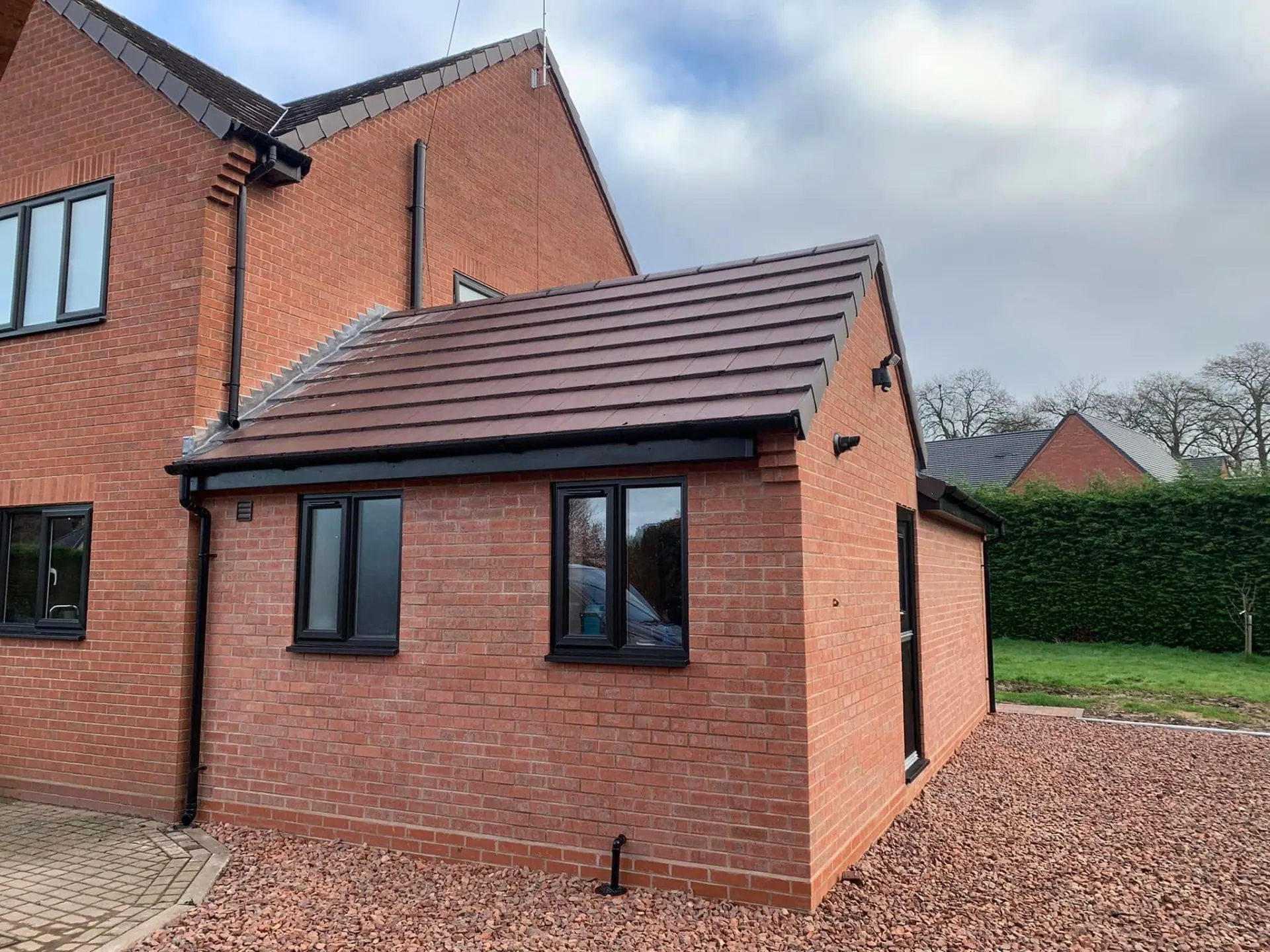 Completed red brick side extension with a brown tiled pitched roof and anthracite windows, built onto a detached house in Worcestershire