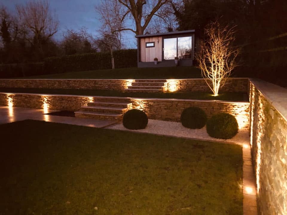 Dry stone garden terraces lit at night with uplighting to the walls, steps and a specimen tree
