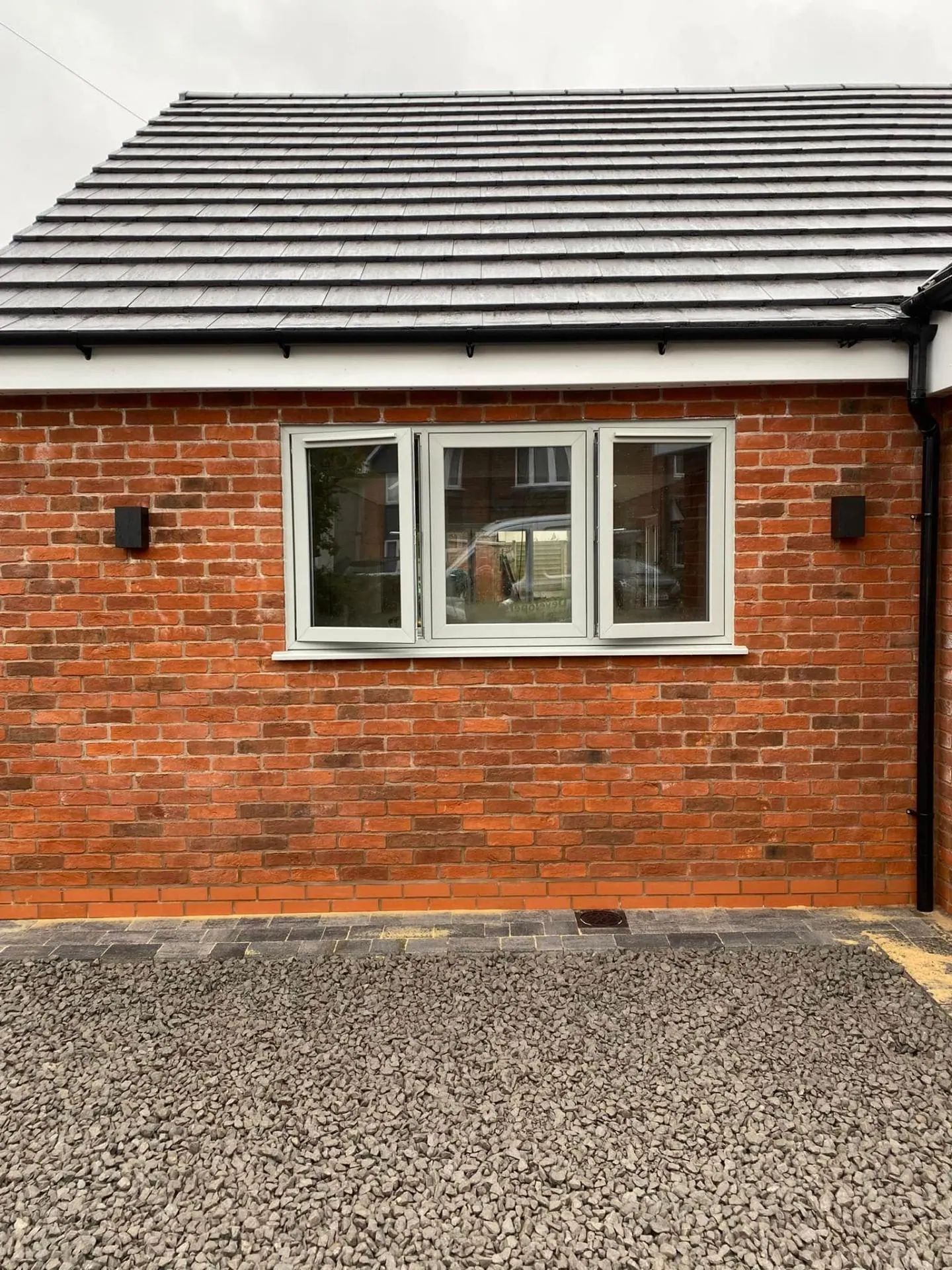 Finished side elevation window at White Gates in agate-grey aluminium frames set into reclaimed-blend red brickwork above a paved and gravel driveway