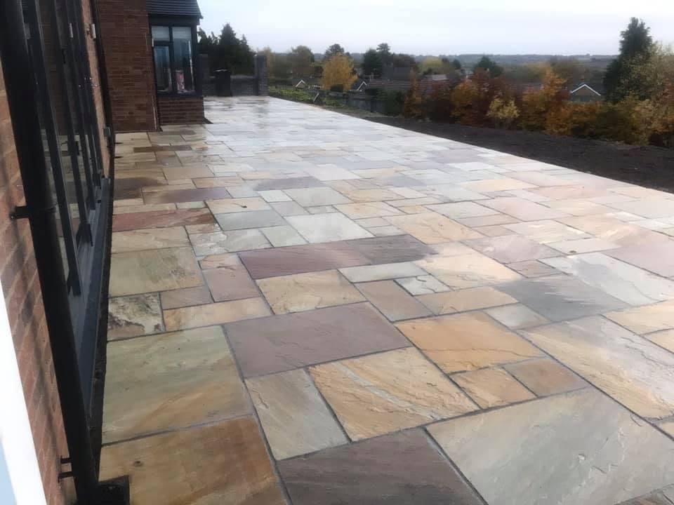 Wide Indian sandstone terrace with riven multi-tone paving running the length of a red brick elevation