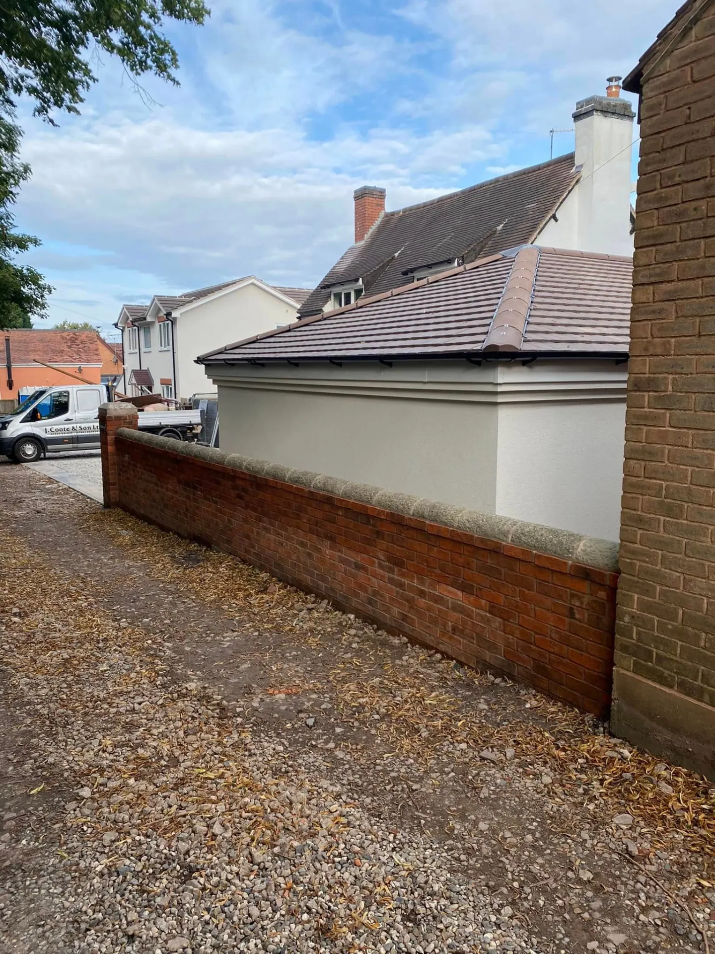 Hipped clay tiled roof and rendered elevation of the new Whiteoaks buildings seen over the reclaimed brick boundary wall