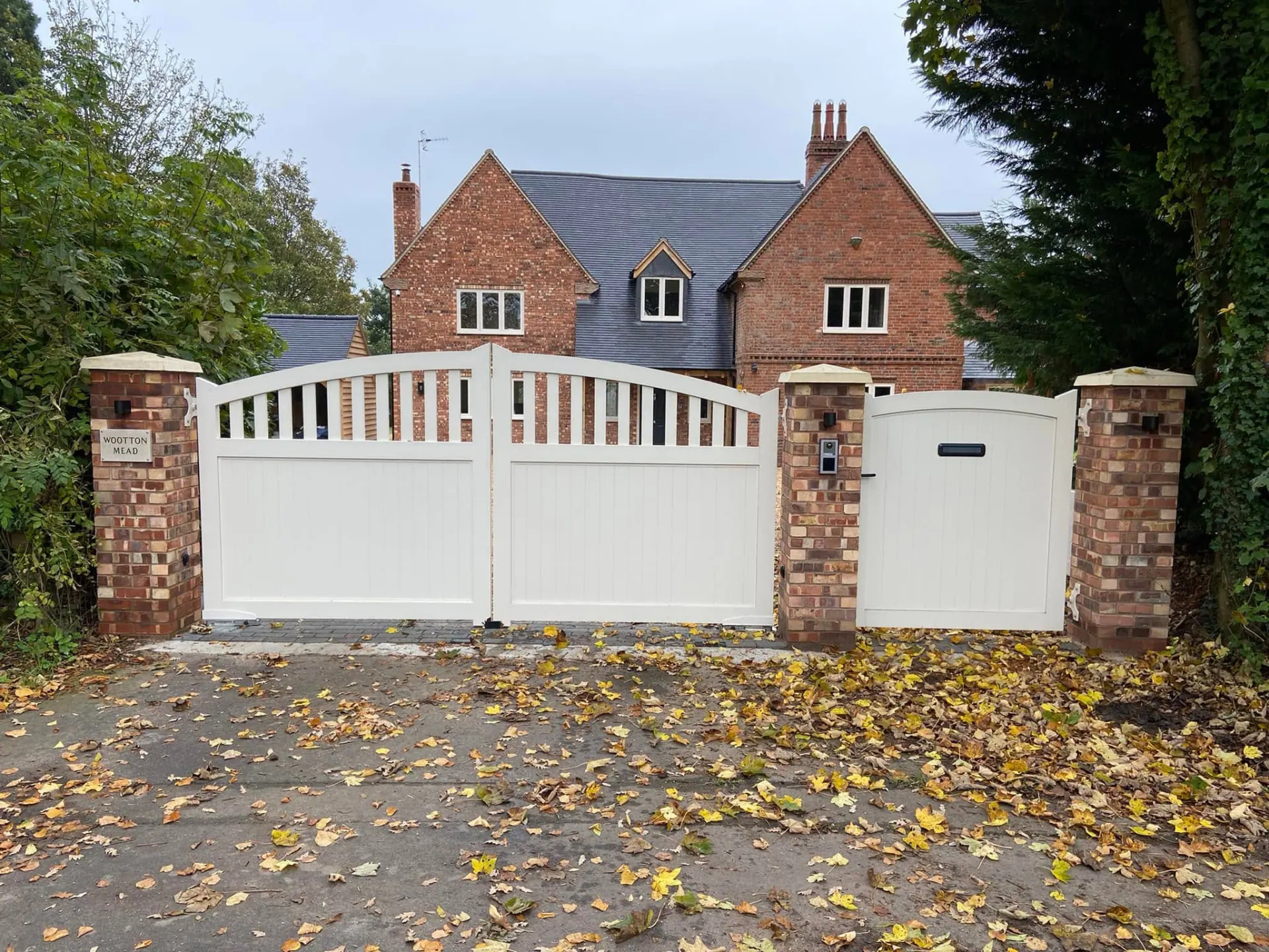 White timber entrance gates, pedestrian gate and brick piers with the completed Wootton Mead house beyond