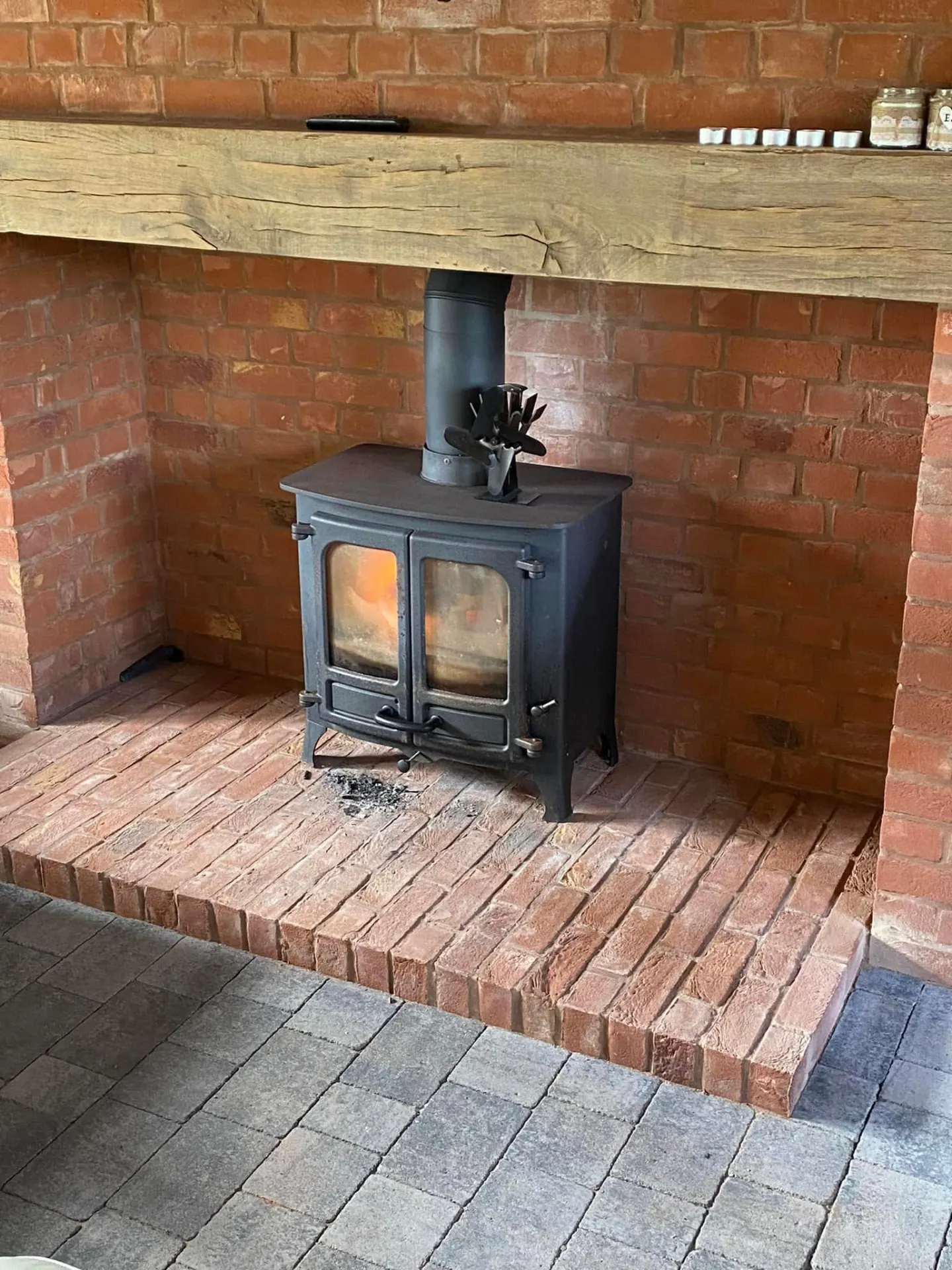 Wood burning stove standing in a red brick niche with a brick hearth and solid oak bressummer beam above