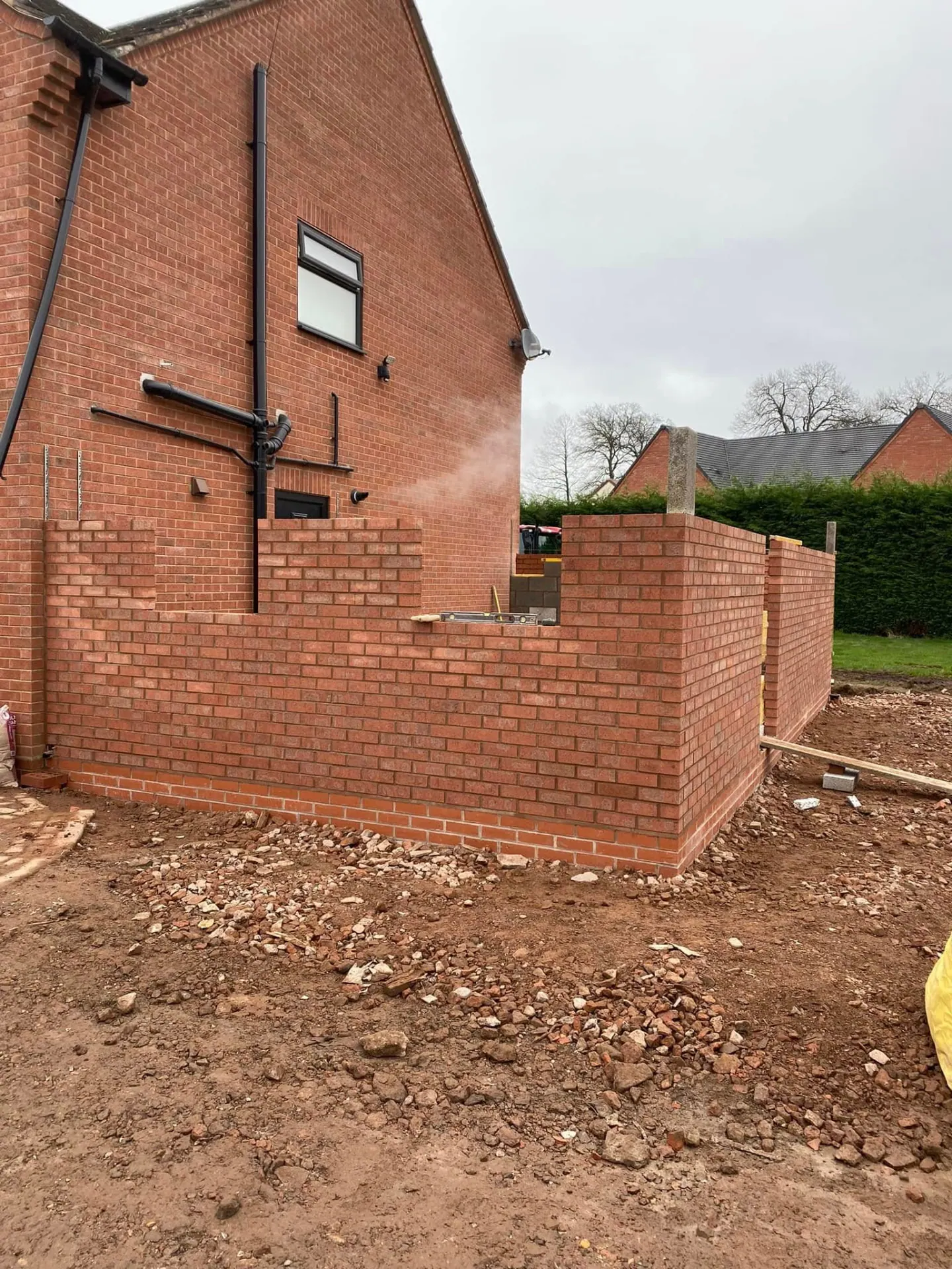 Side extension brickwork rising above damp proof course level with corner piers and a spirit level on the wall head