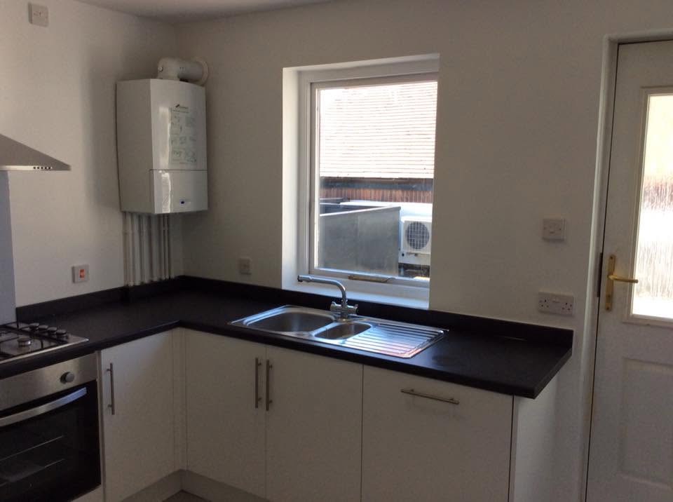 Staff kitchen corner with stainless sink under a window, dark worktop, white units and a wall-mounted boiler
