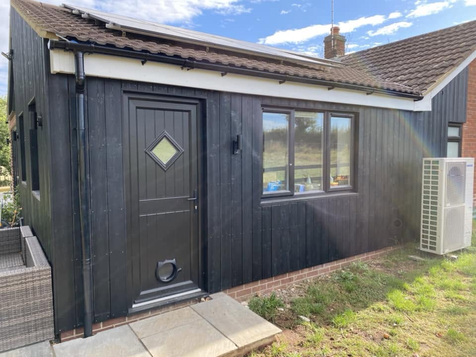 Side entrance with dark composite door, black vertical cladding, utility window and air source heat pump unit