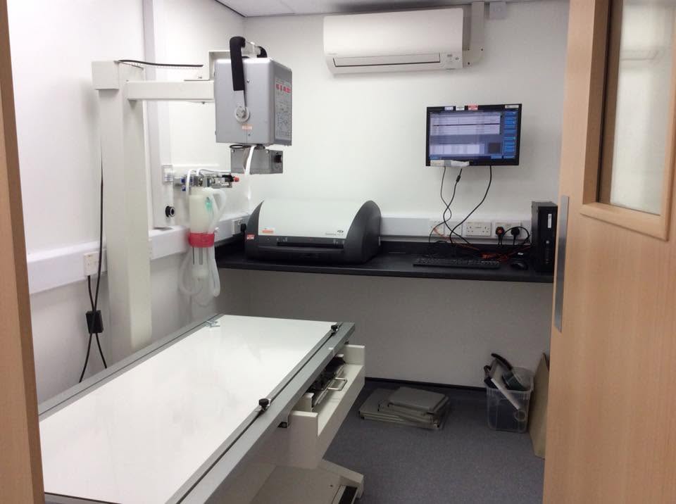 Veterinary imaging room with wall-mounted X-ray gantry, radiography table, digital processor and console on a fitted worktop