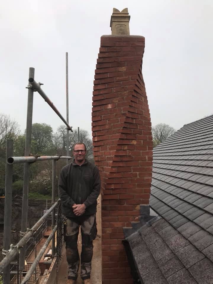 Bricklayer standing next to the twisted-brick chimney stack at the Inkberrow new-build