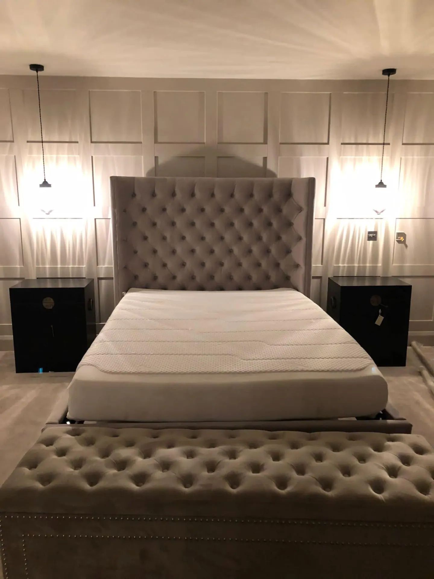 Panelled principal bedroom with upholstered bed, bench seating and pendant lights either side of the headboard