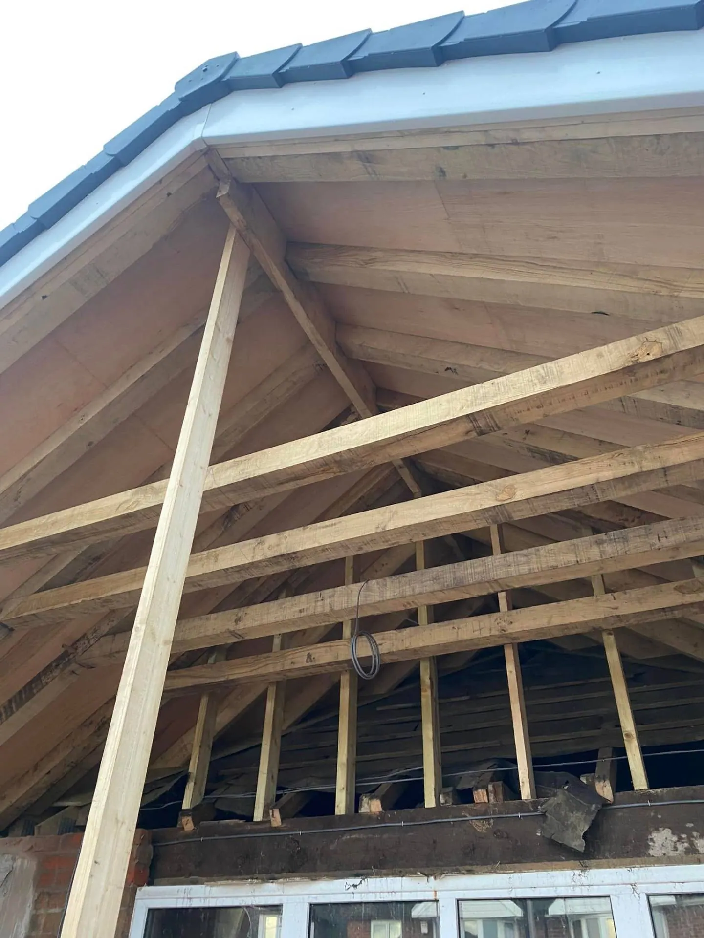 Looking up into the hand-cut oak-toned roof carpentry over the new rear gable at White Gates from below, with fresh dry ridge and slate details above
