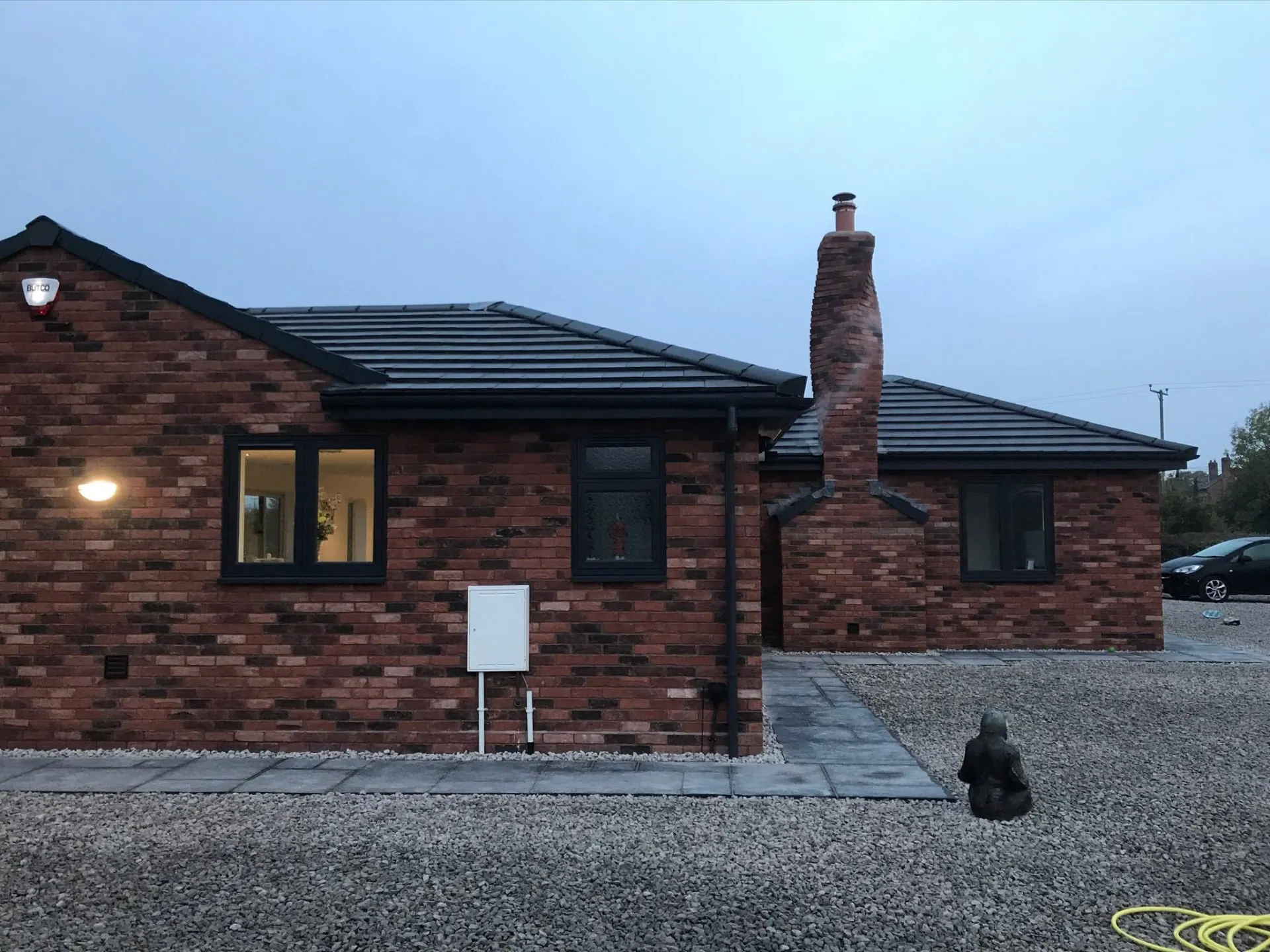 JRC-built new-build brick bungalow in Worcestershire with a hipped grey tiled roof, anthracite windows and a hand-laid twisted brick chimney stack at dusk