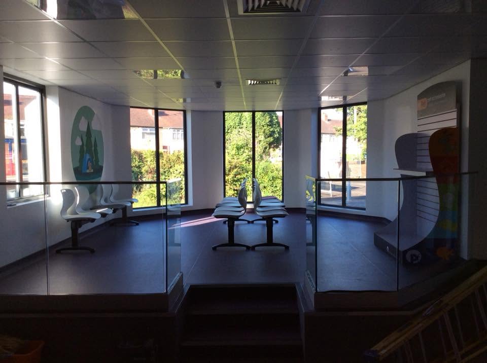 Split-level veterinary waiting area with frameless glass balustrades, bay windows, moulded seating benches and wall graphics