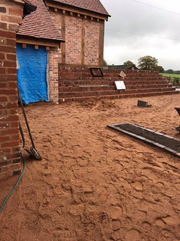 Brick terracing and steps built up to the new oak-framed garden room at the listed farmhouse, with the terrace sub-base prepared for paving