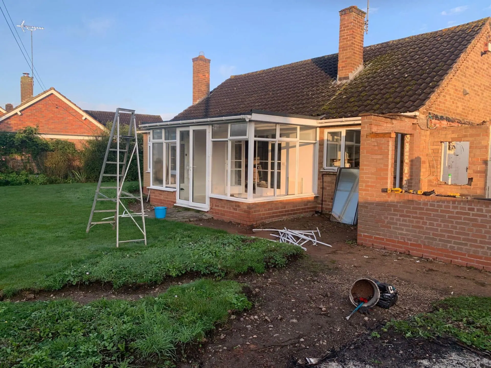 Existing rear conservatory and stripped-back gable at White Gates before demolition, with ladder and tools on the lawn