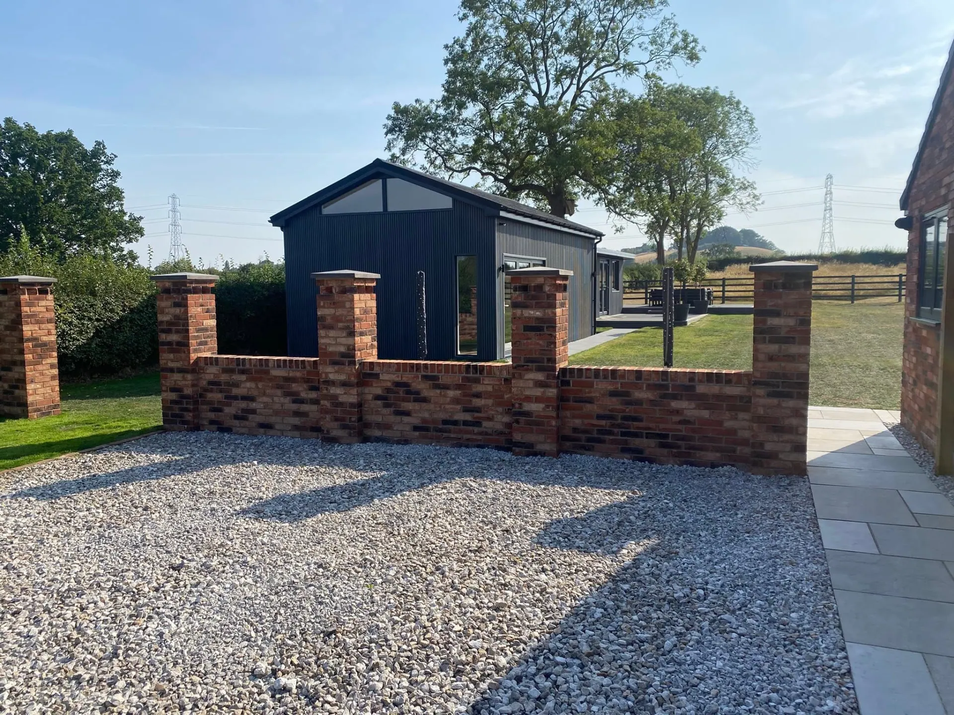 Wide view of the golf swing room behind new red brick boundary walls with brick-on-edge coping and capped pillars on a light gravel driveway