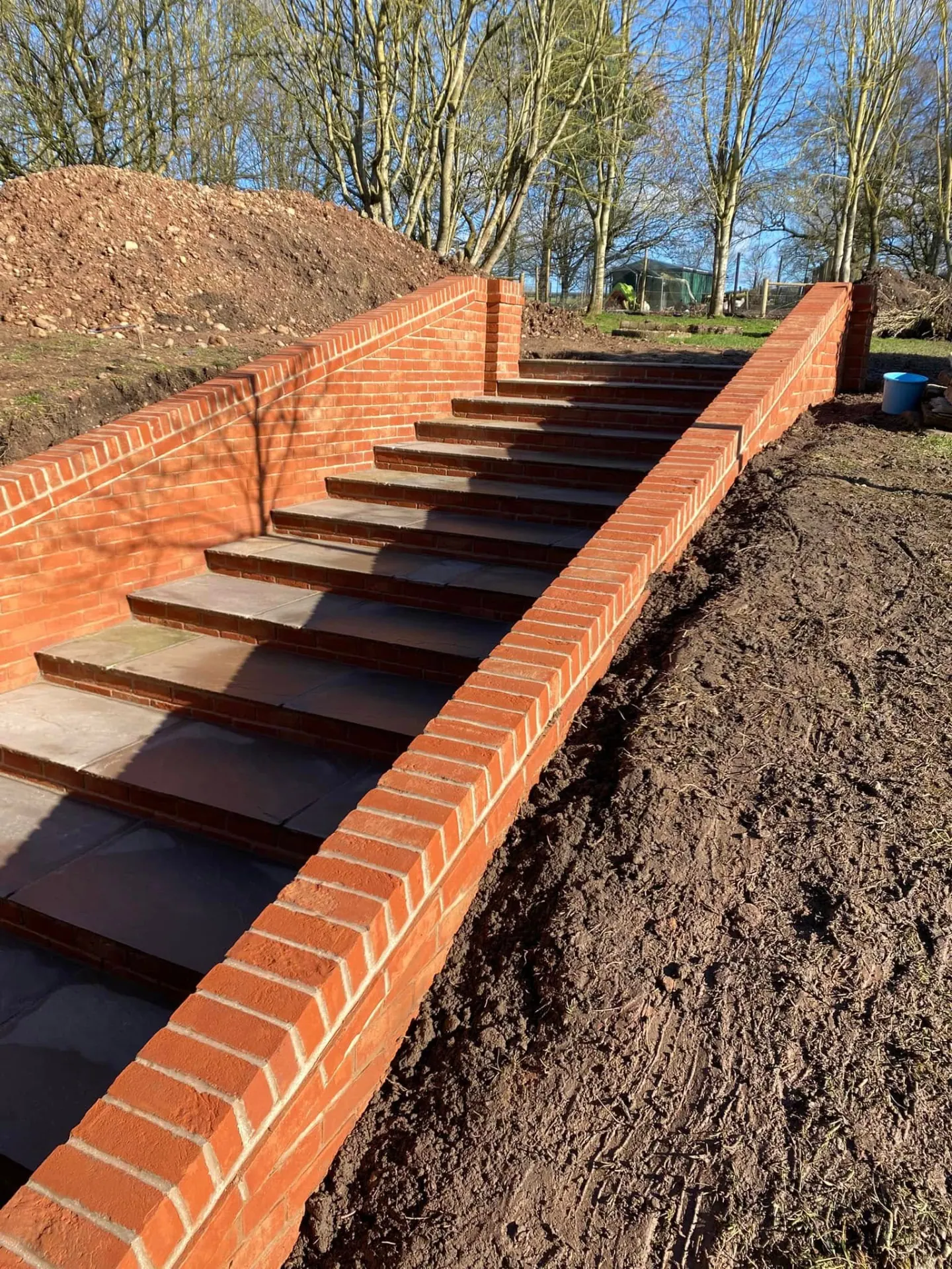 Completed flight of red brick steps with Indian sandstone treads and raking brick-on-edge coping climbing a garden bank