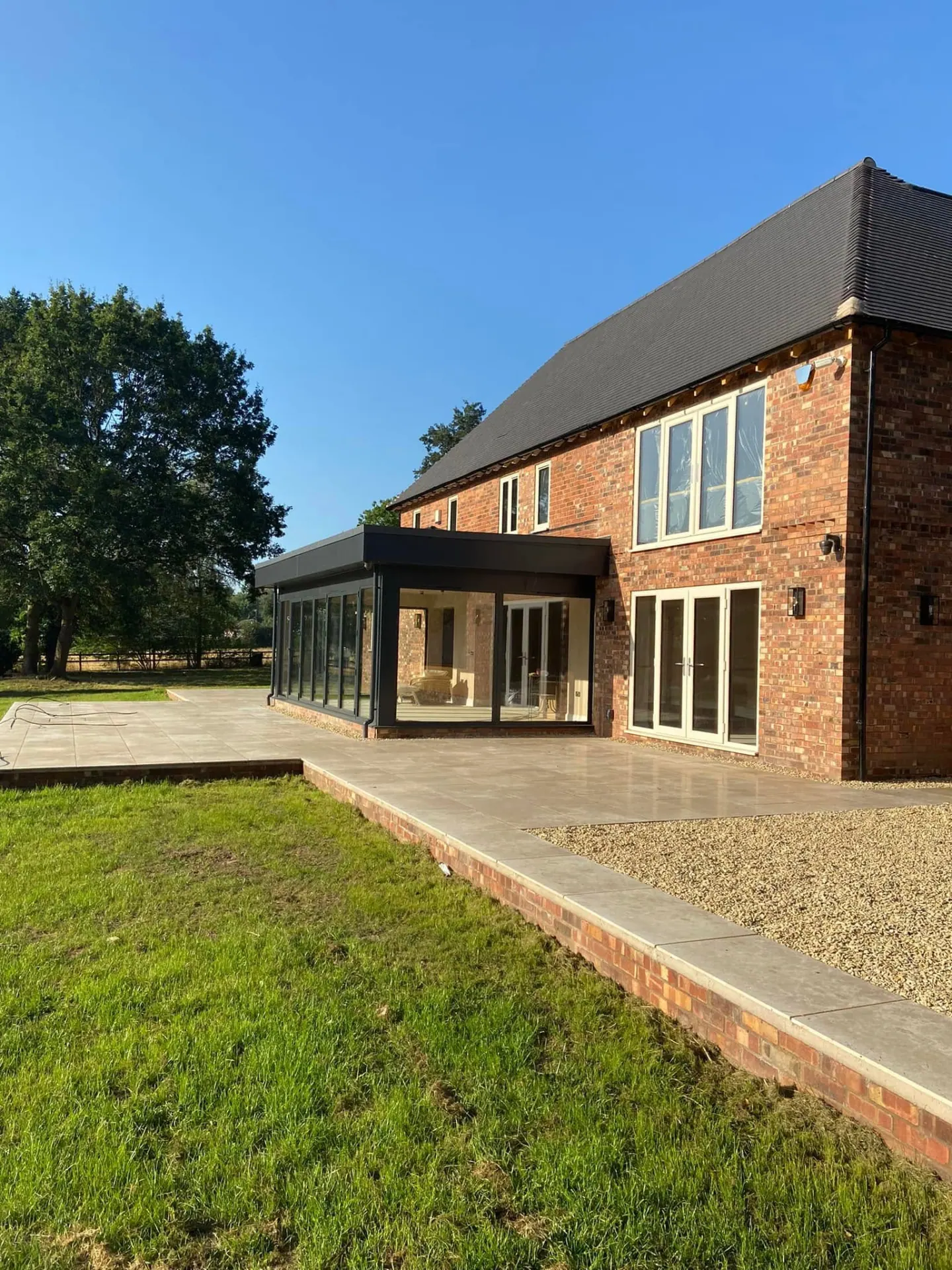 Angled rear garden view of the completed house and terrace with the new glazed extension catching the sun
