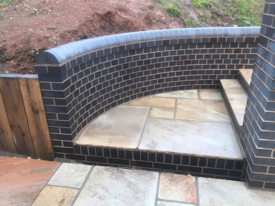 Curved blue brick retaining wall with bullnose coping beside a sandstone terrace — specialist brickwork by JRC Developers