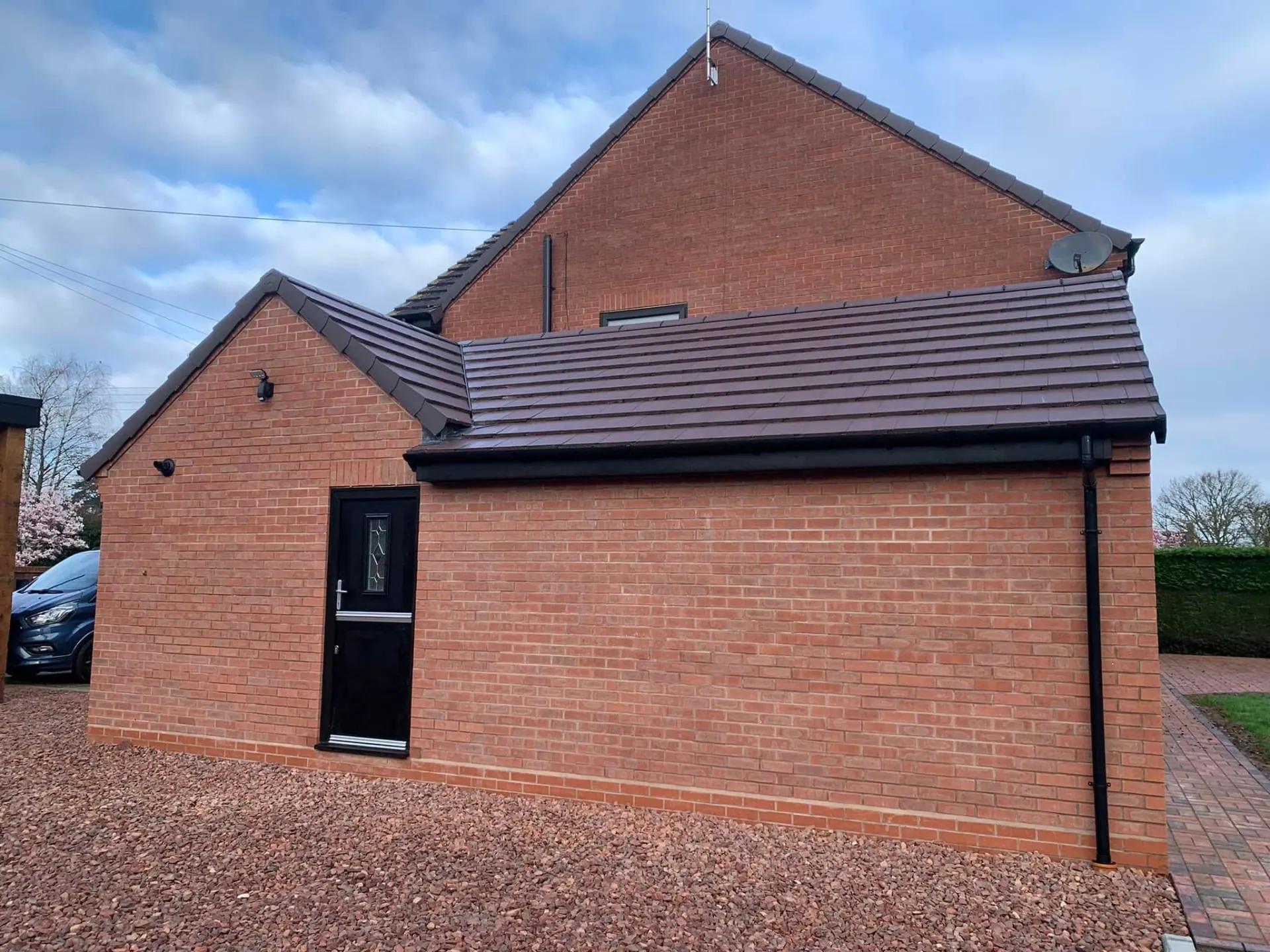 Completed side extension seen from the driveway showing the tiled roof, brickwork and new gravel and block paved surfaces