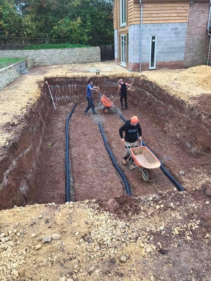 Crew laying pool pipework and drainage runs in gravel within the pool excavation