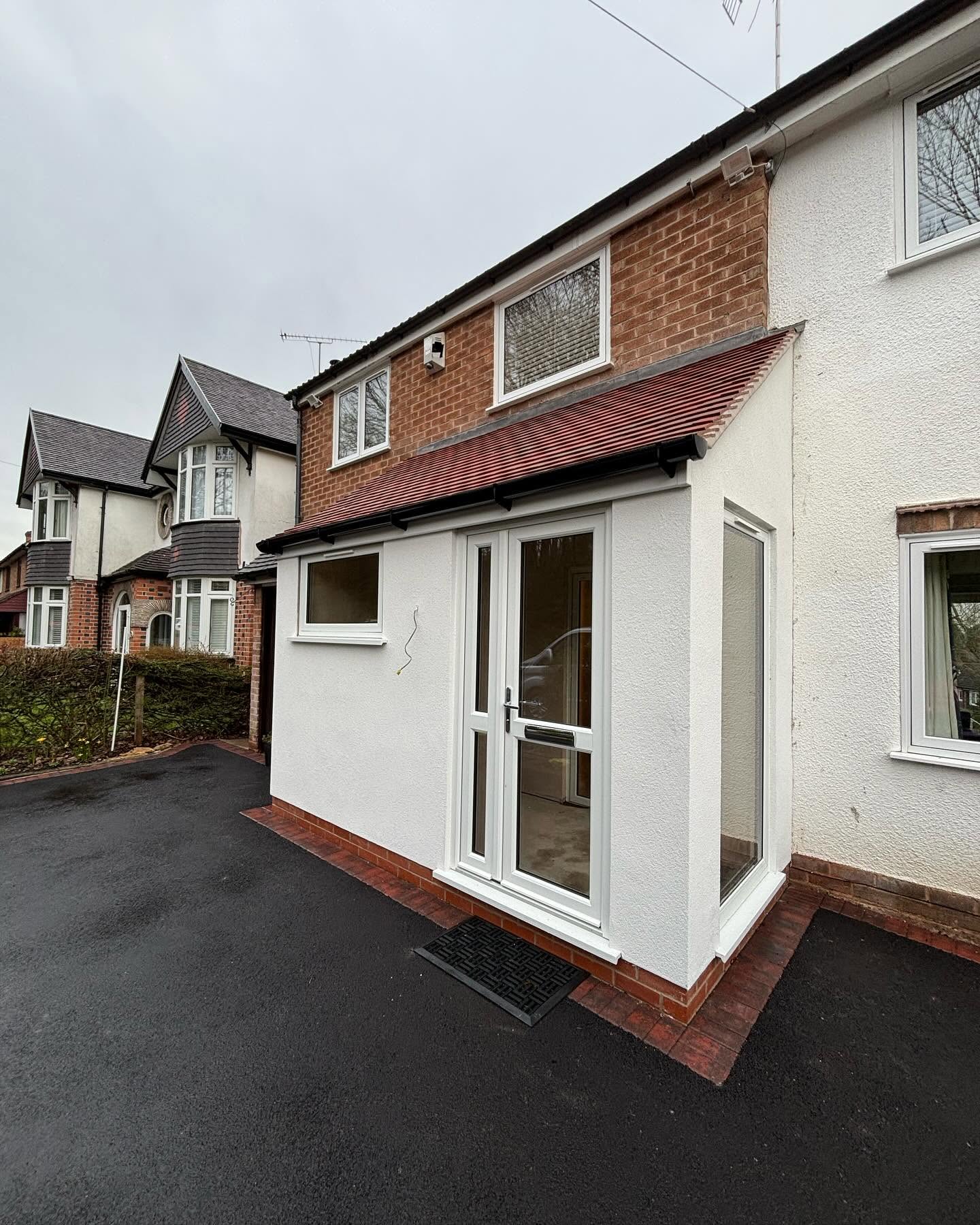 Completed rendered porch with red brick plinth, clay tiled roof and white uPVC French doors alongside a new brick-edged tarmac double driveway in Redditch, built by JRC Developers
