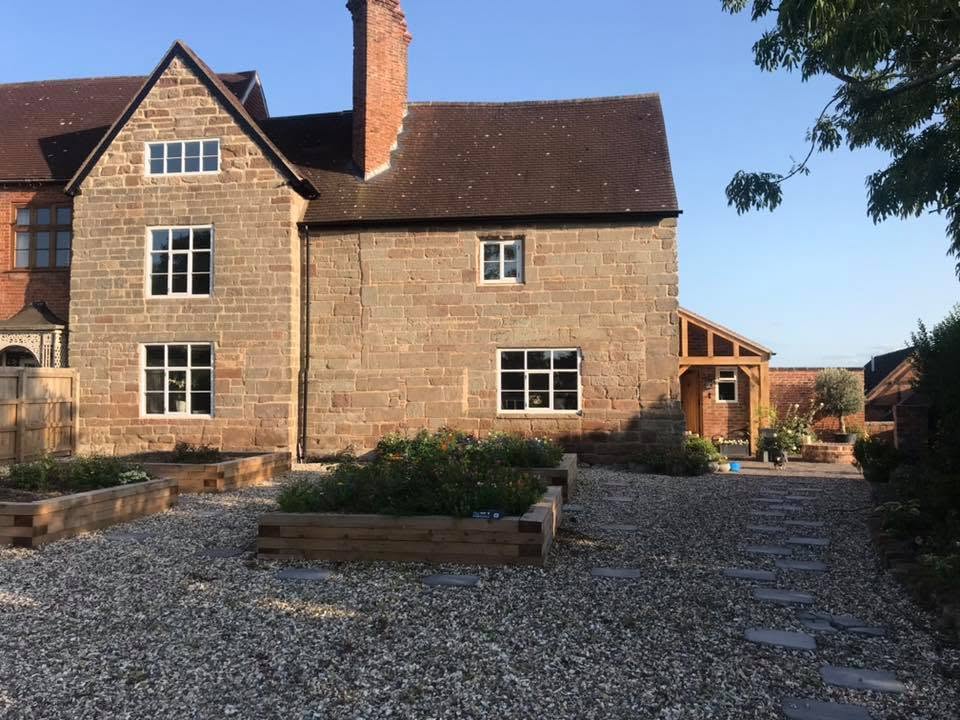 Restored Grade II listed sandstone farmhouse in Worcestershire with repointed stonework, new clay tiled roof, oak-framed porch, gravel courtyard and raised sleeper beds — restored by JRC Developers