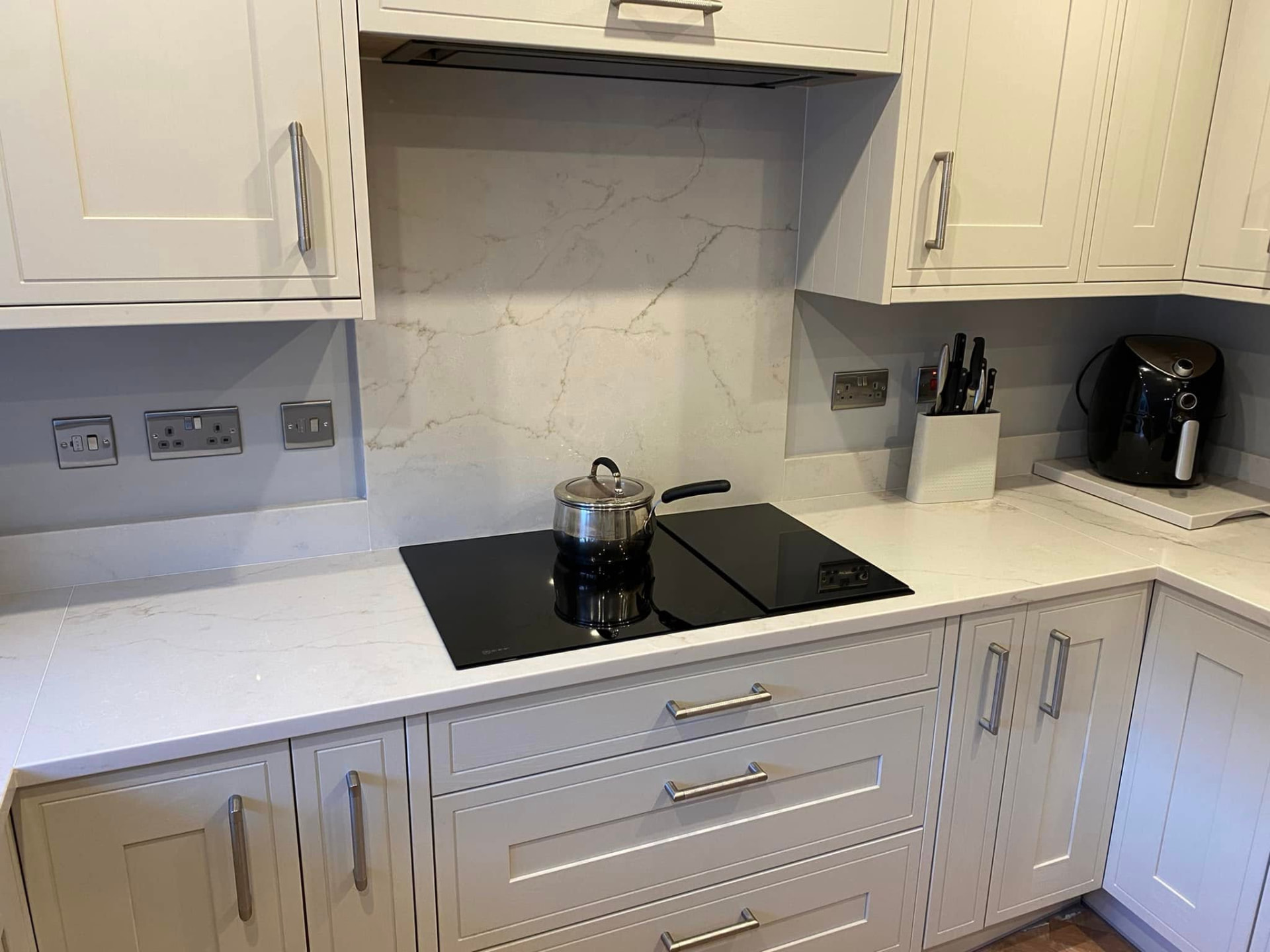 Detail of the veined quartz worktop, full-height quartz splashback, induction hob and recessed extractor in the new kitchen